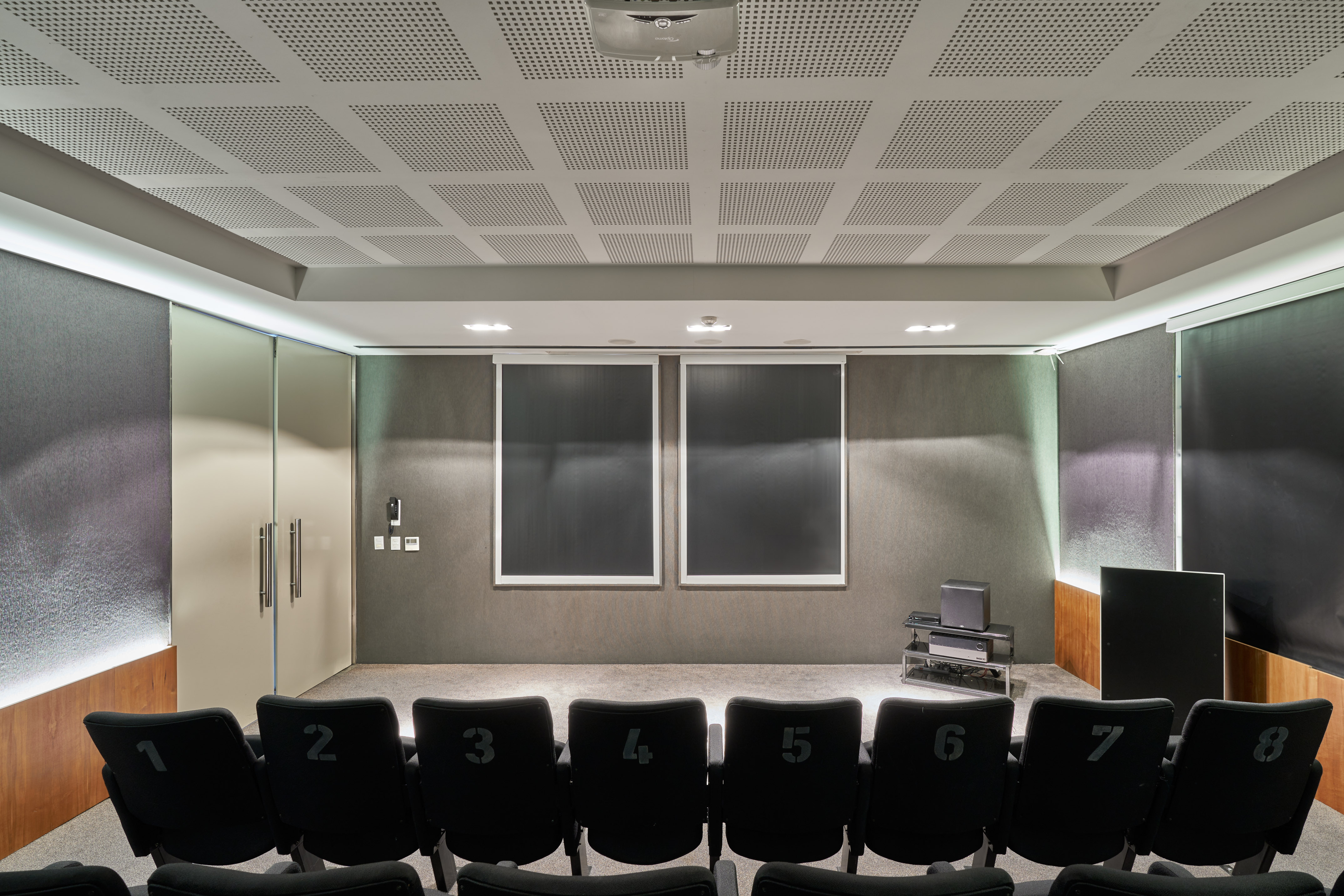 Modern screening room with numbered seats, ceiling projector, and acoustic panels.