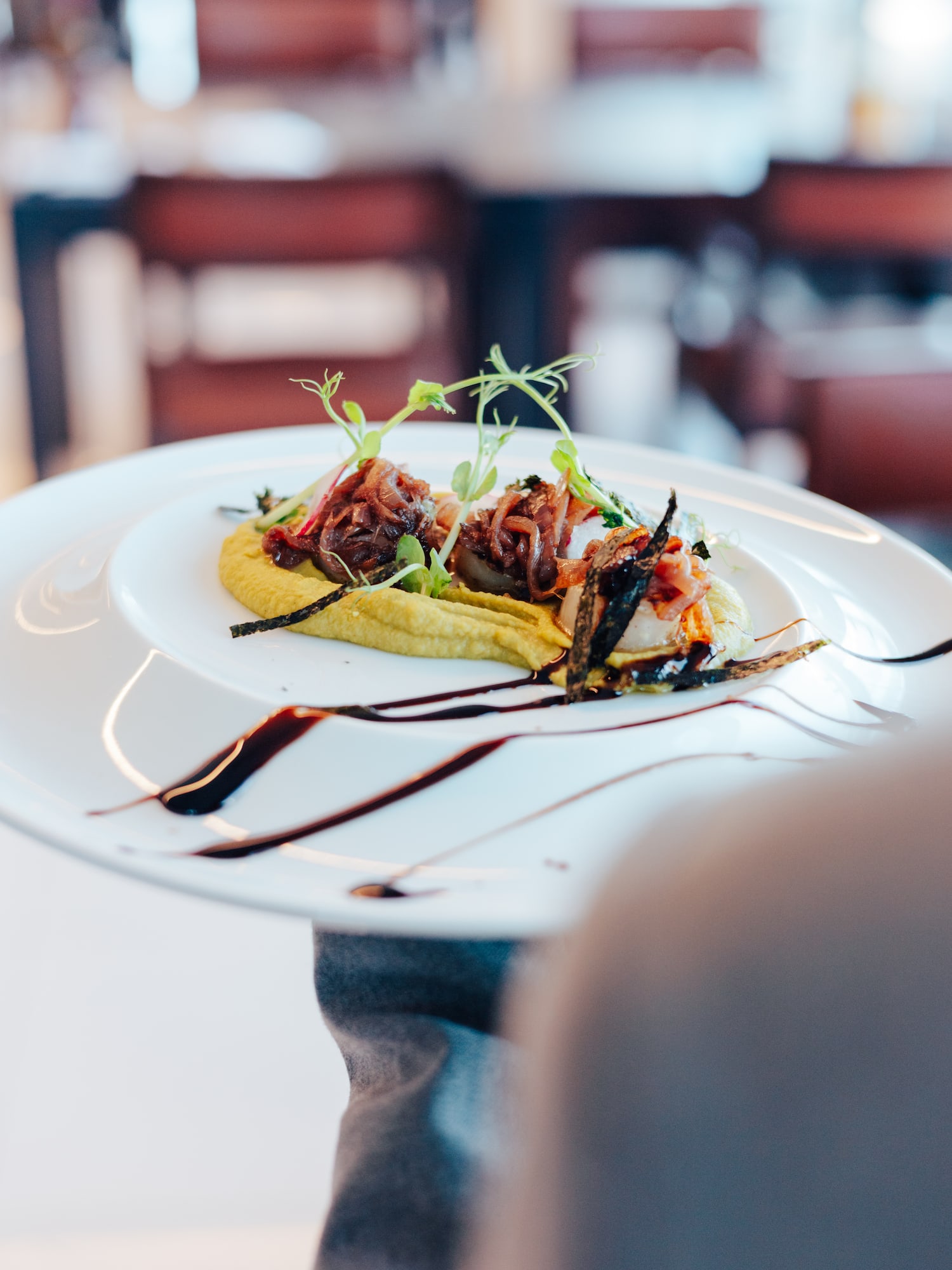 Plated gourmet dish with caramelized onions, yellow puree, and microgreens.