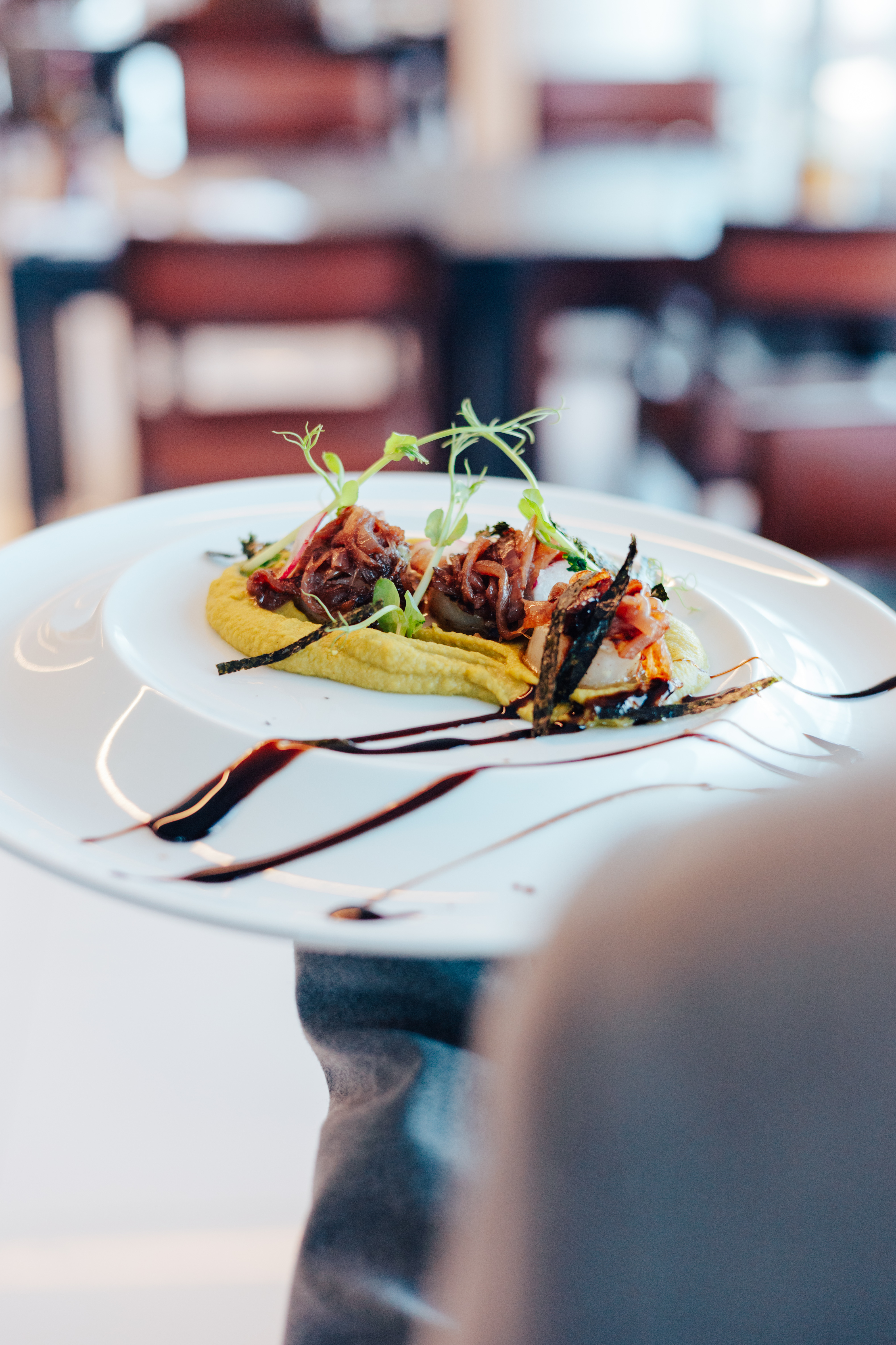 Plated gourmet dish with caramelized onions, yellow puree, and microgreens.