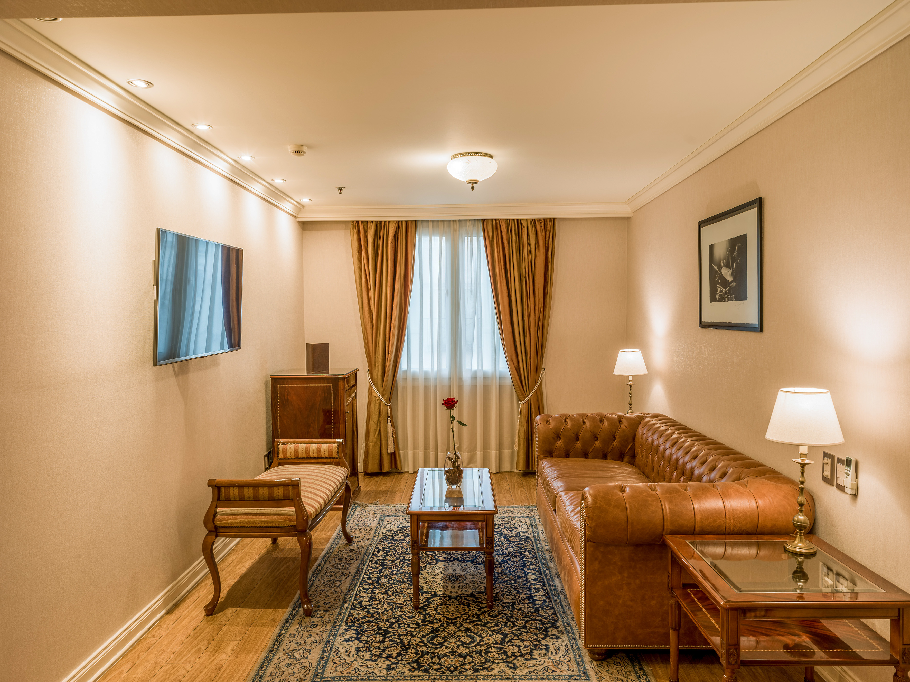 Luxury hotel suite with brown Chesterfield sofa, wooden furniture, and rug.