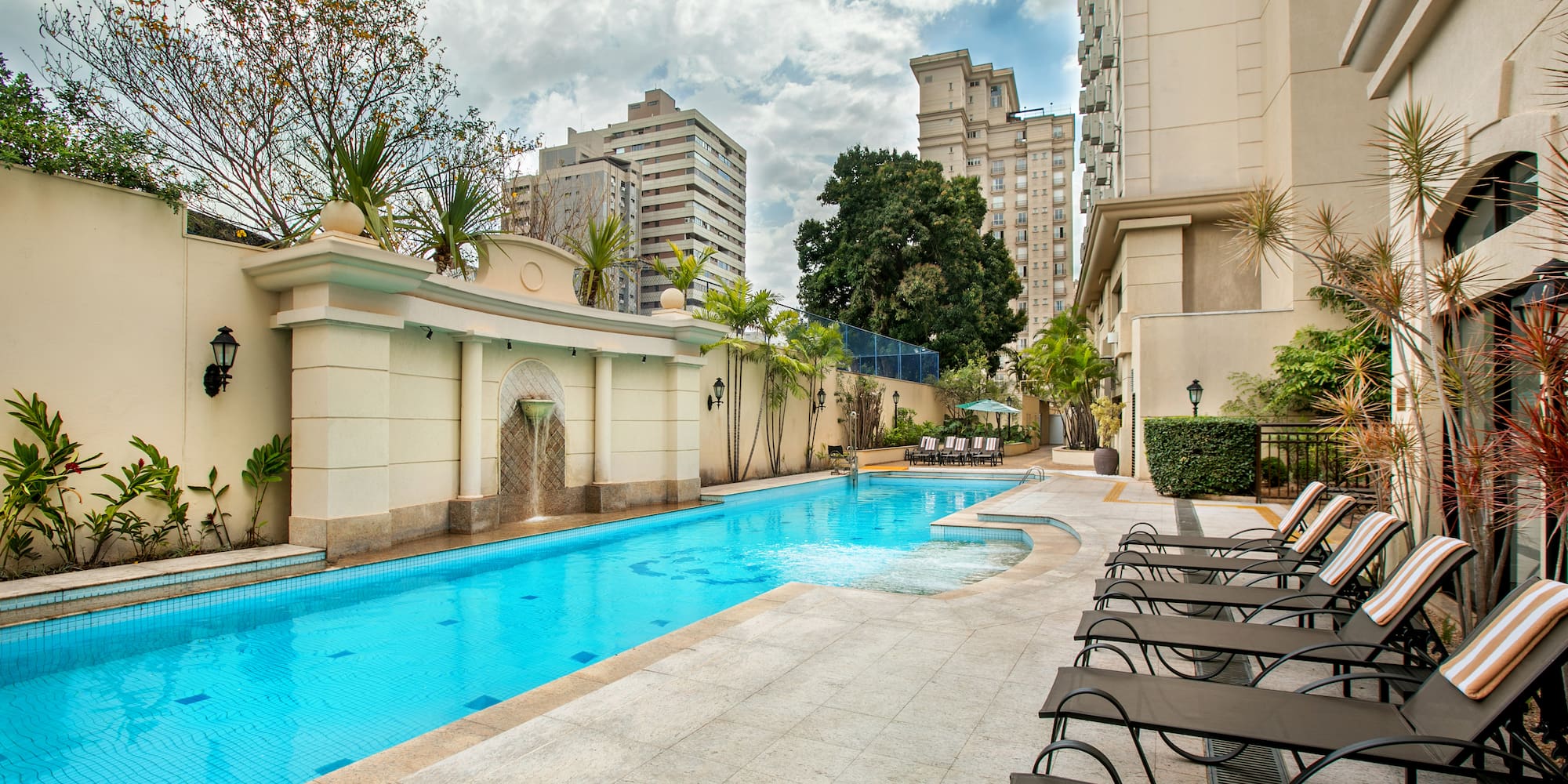 a pool with chairs and a fountain in the background