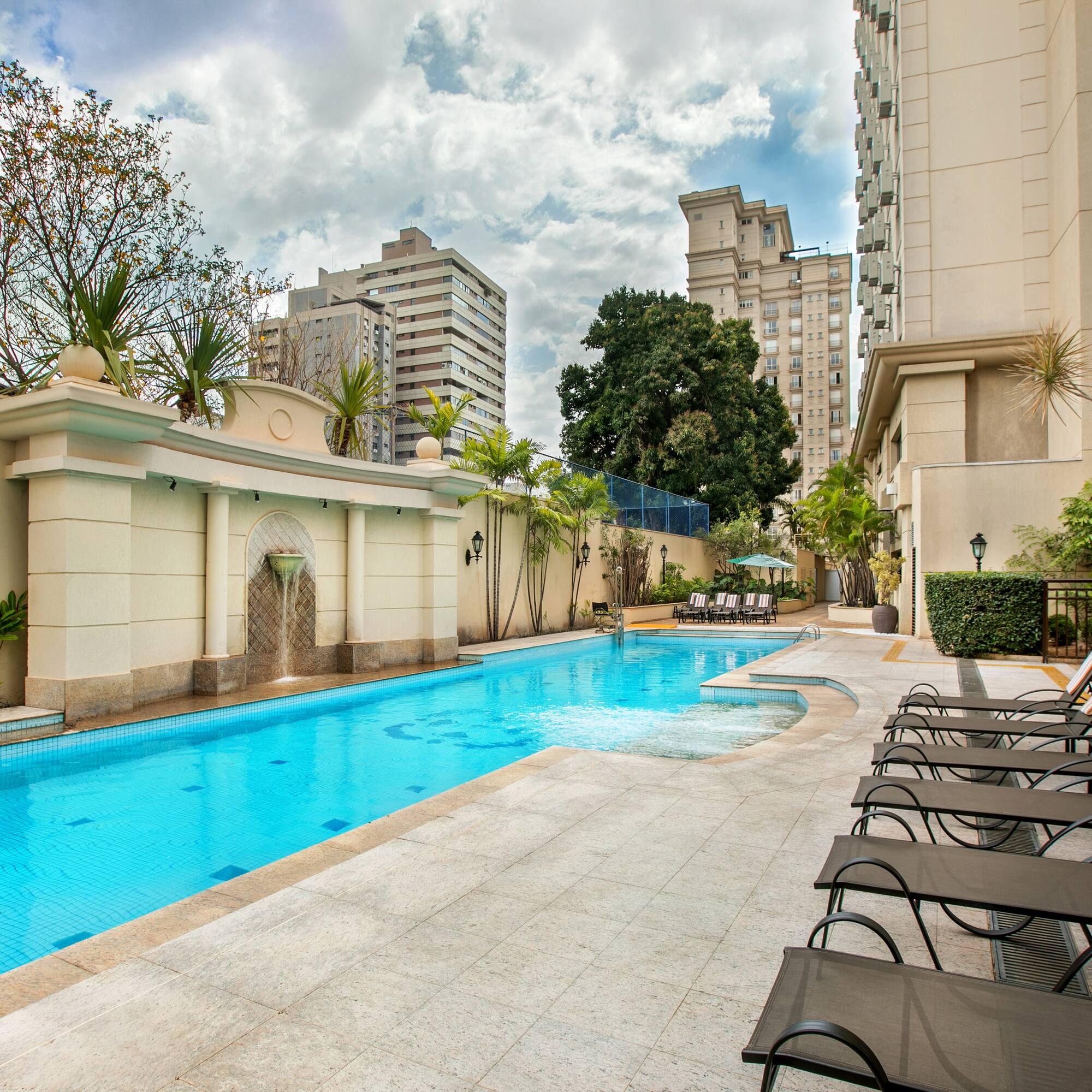 a pool with chairs and a fountain in the background