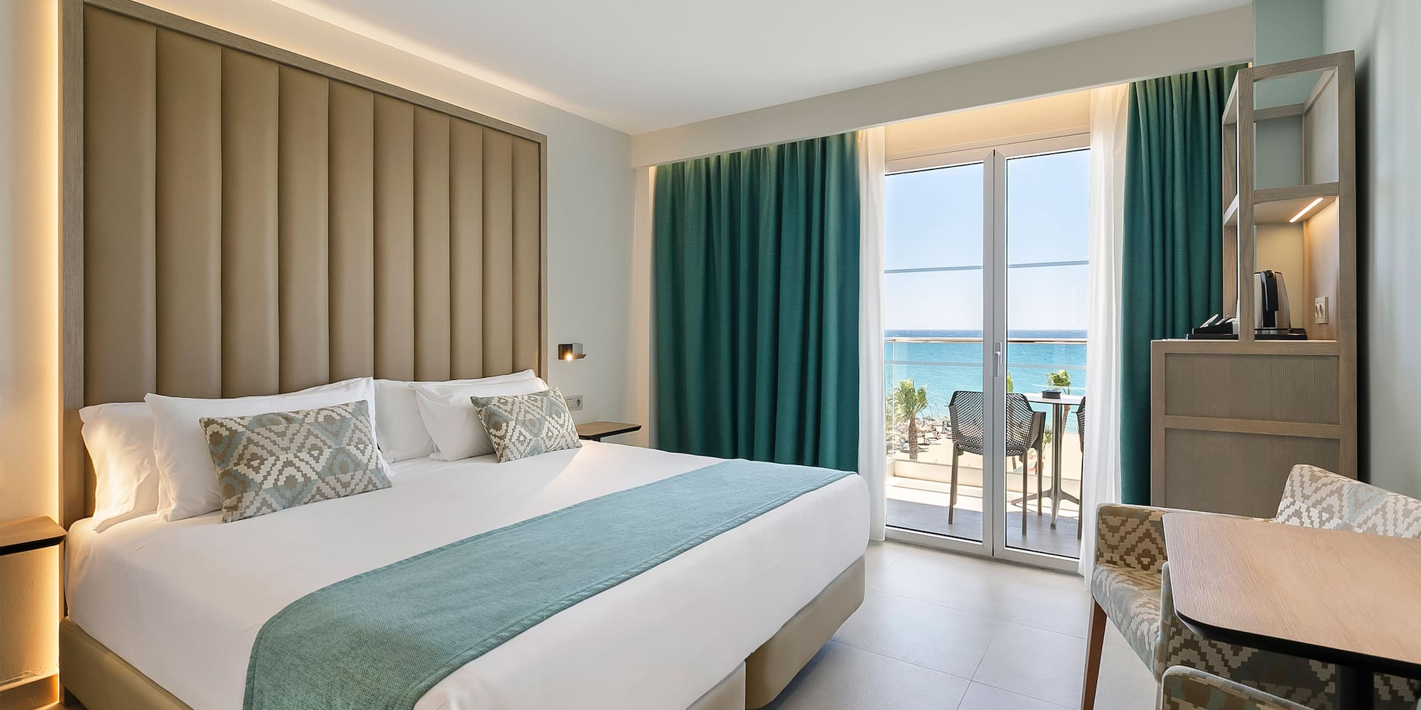 a room with a bed and chairs and a table with a view of the ocean