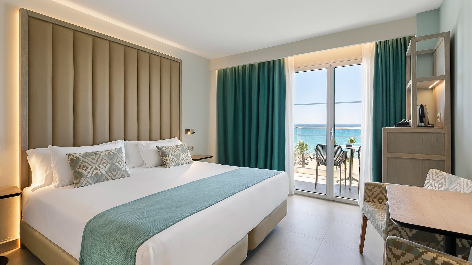 a room with a bed and chairs and a table with a view of the ocean