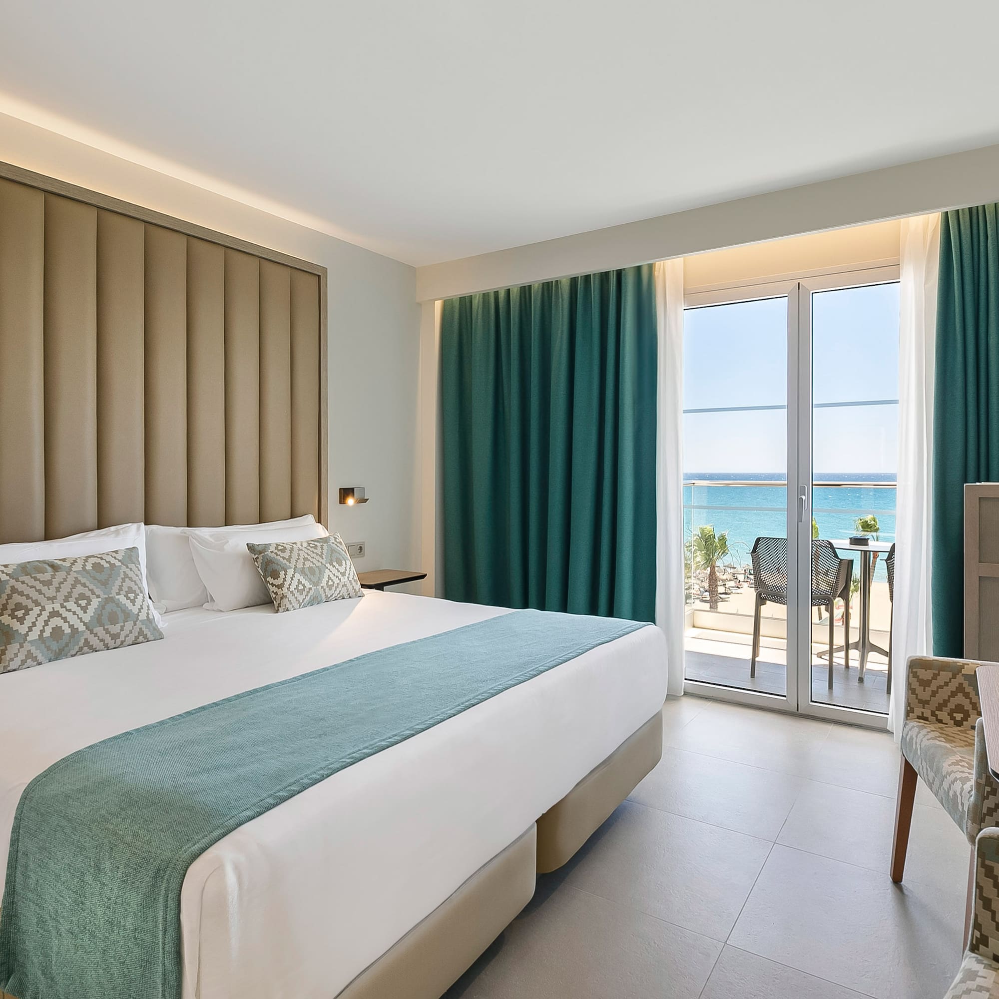 a room with a bed and chairs and a table with a view of the ocean