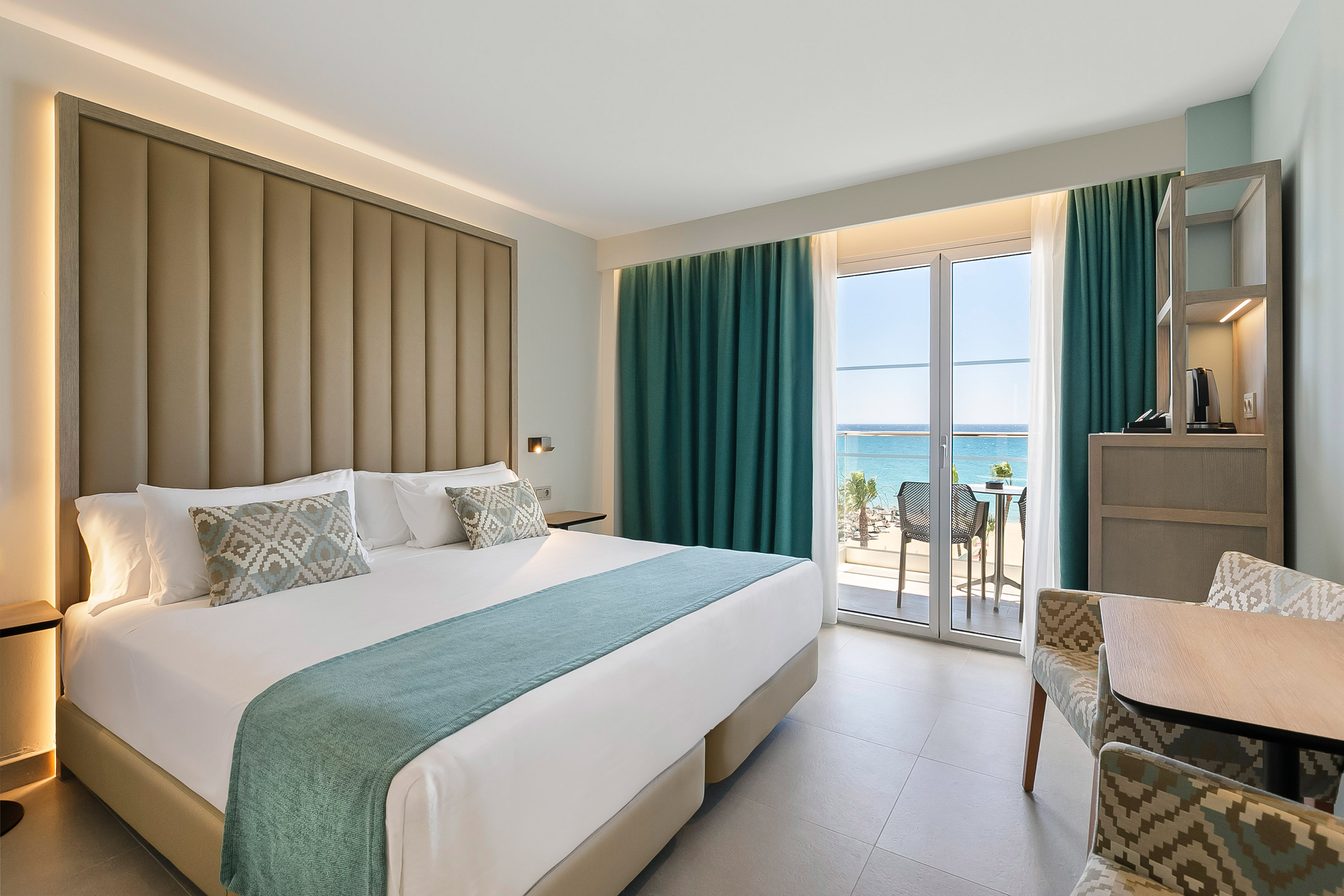 Modern hotel room with ocean view, king bed, balcony, and teal accents.