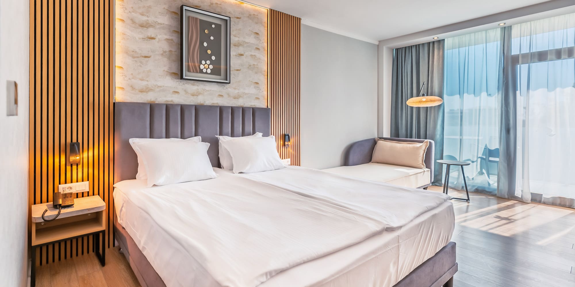 Modern hotel room with large bed, wood paneling, and balcony access.