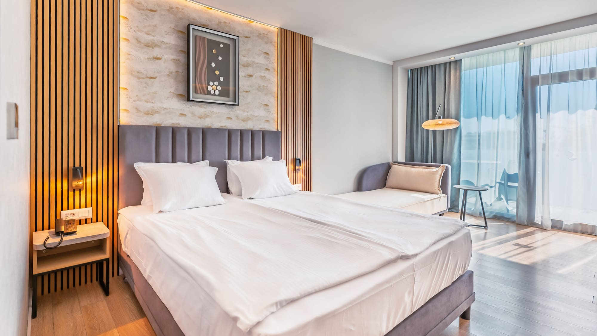 Modern hotel room with large bed, wood paneling, and balcony access.