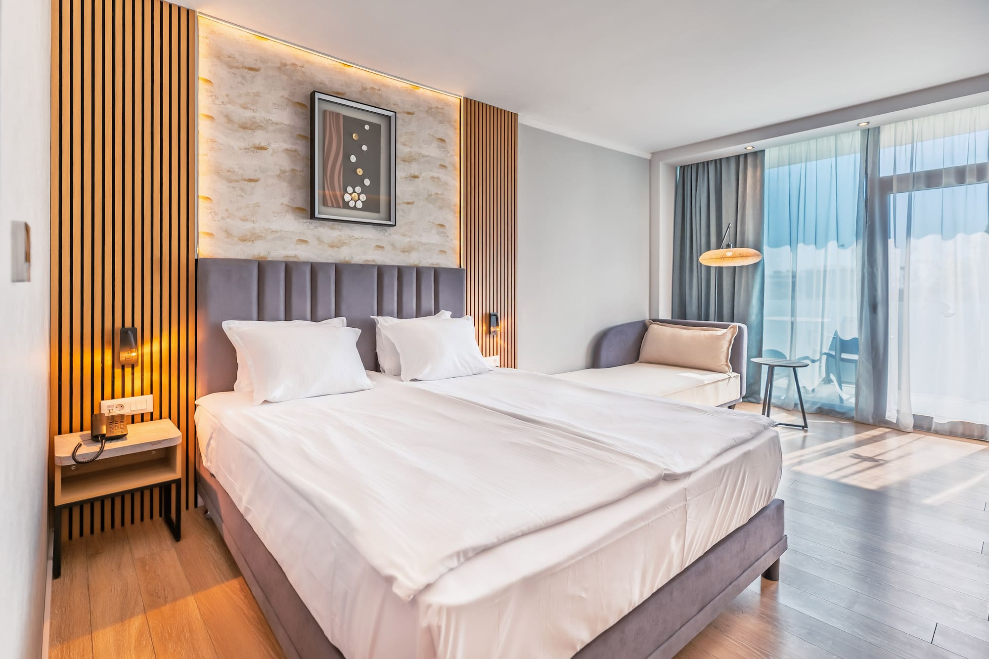 Modern hotel room with large bed, wood paneling, and balcony access.