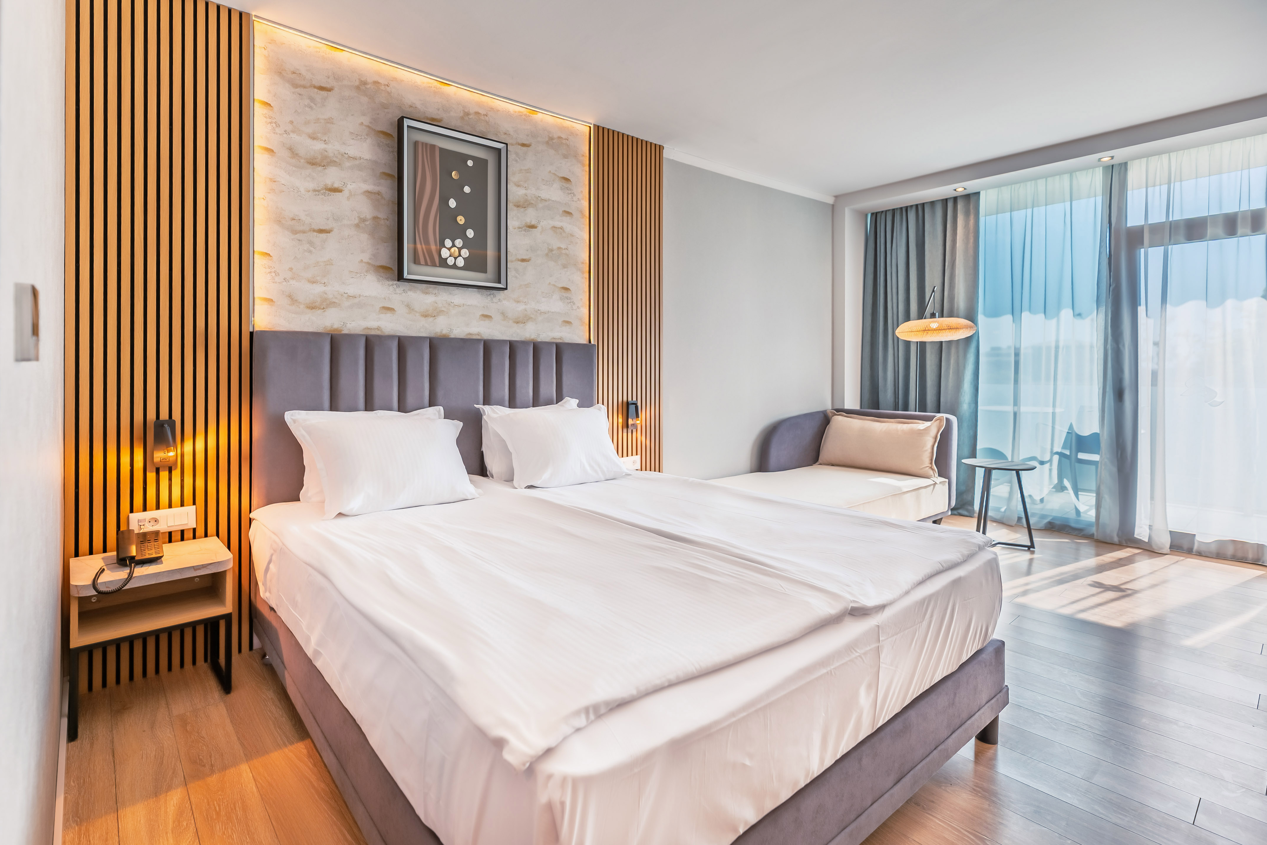 Modern hotel room with large bed, wood paneling, and balcony access.