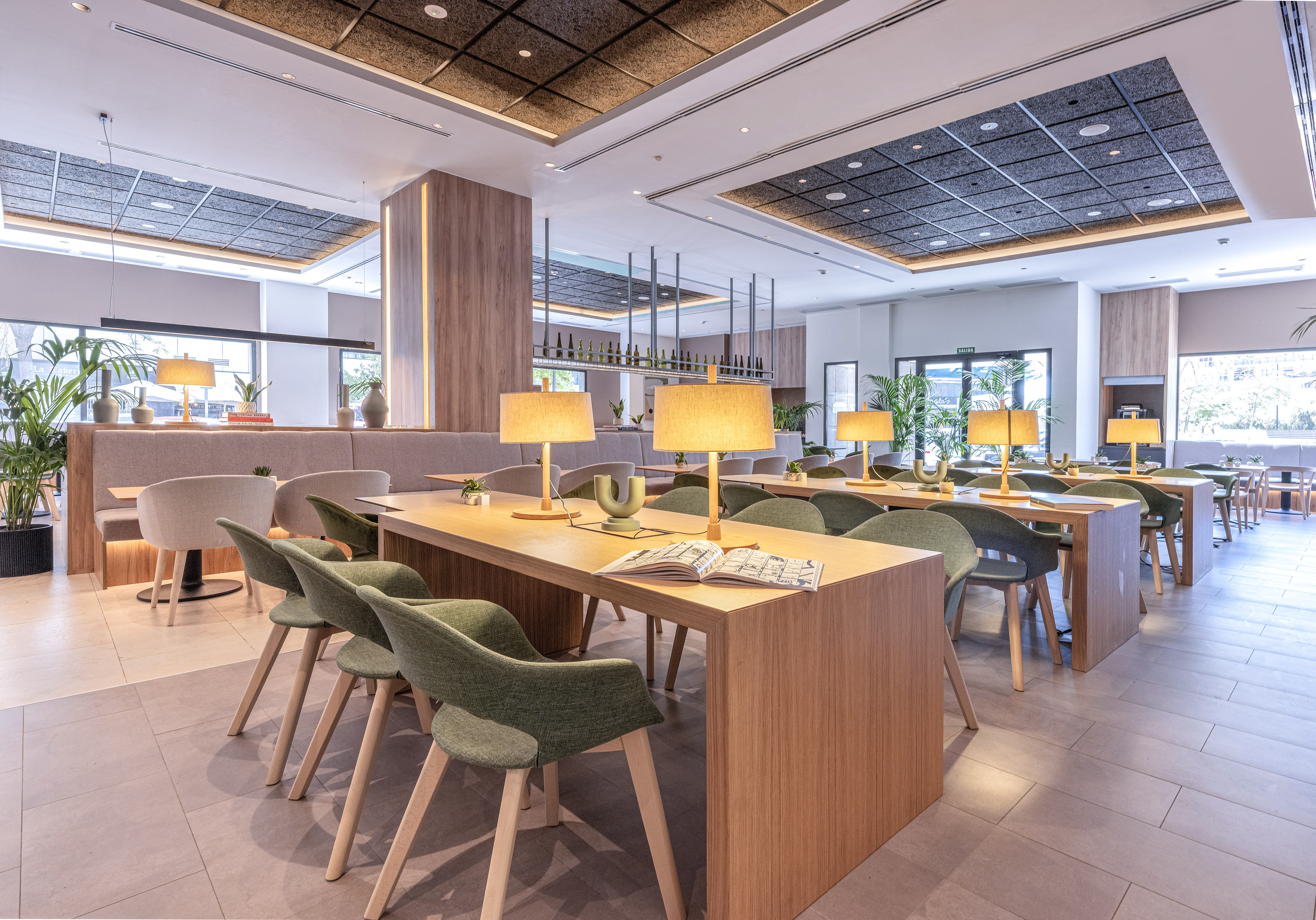 Modern cafe interior with long wooden tables, green chairs, and warm lamps.