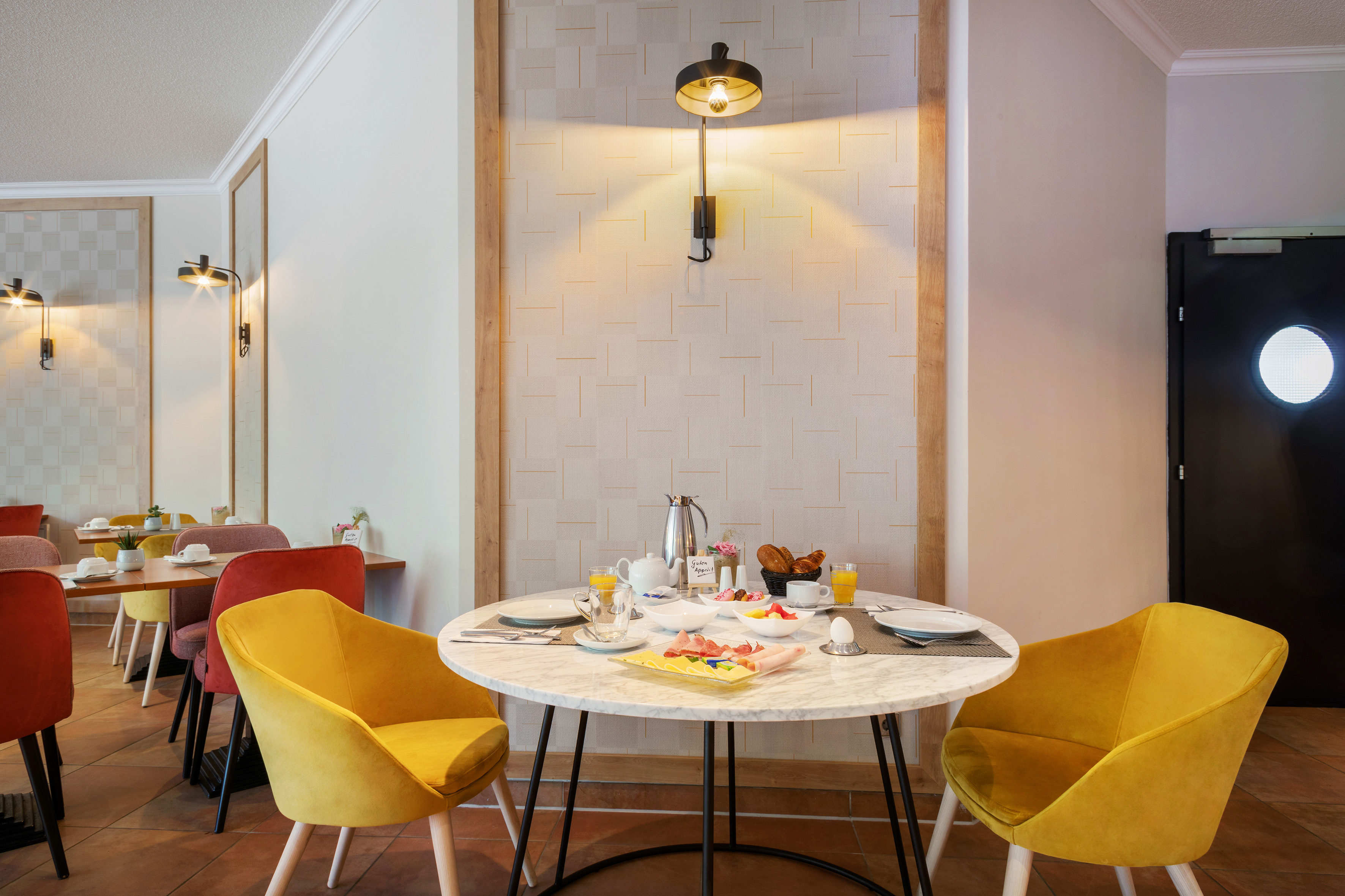 Hotel breakfast table with food, juice, and yellow chairs in a warm dining area.