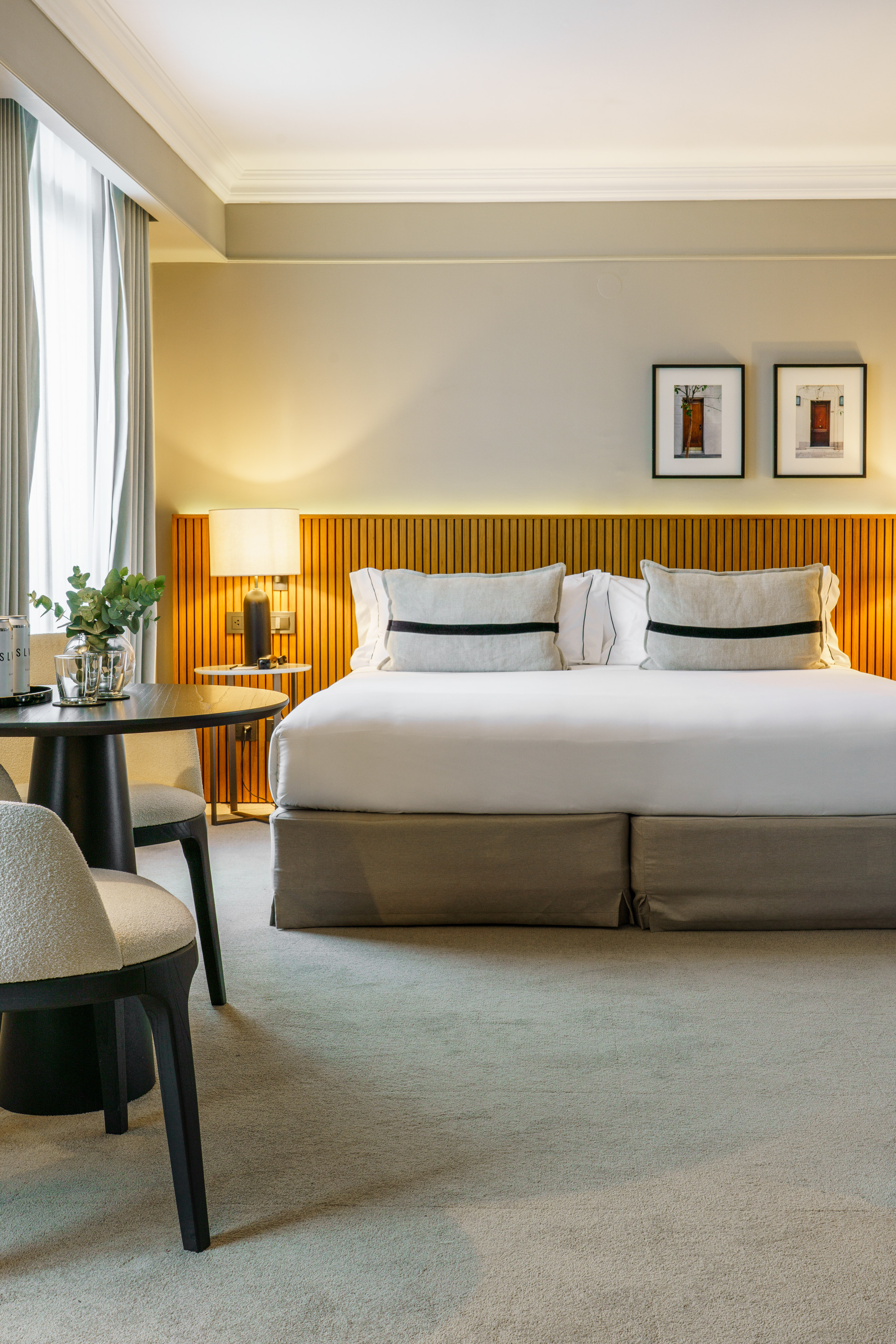 Modern hotel room with large bed, wooden headboard, art, and seating area.
