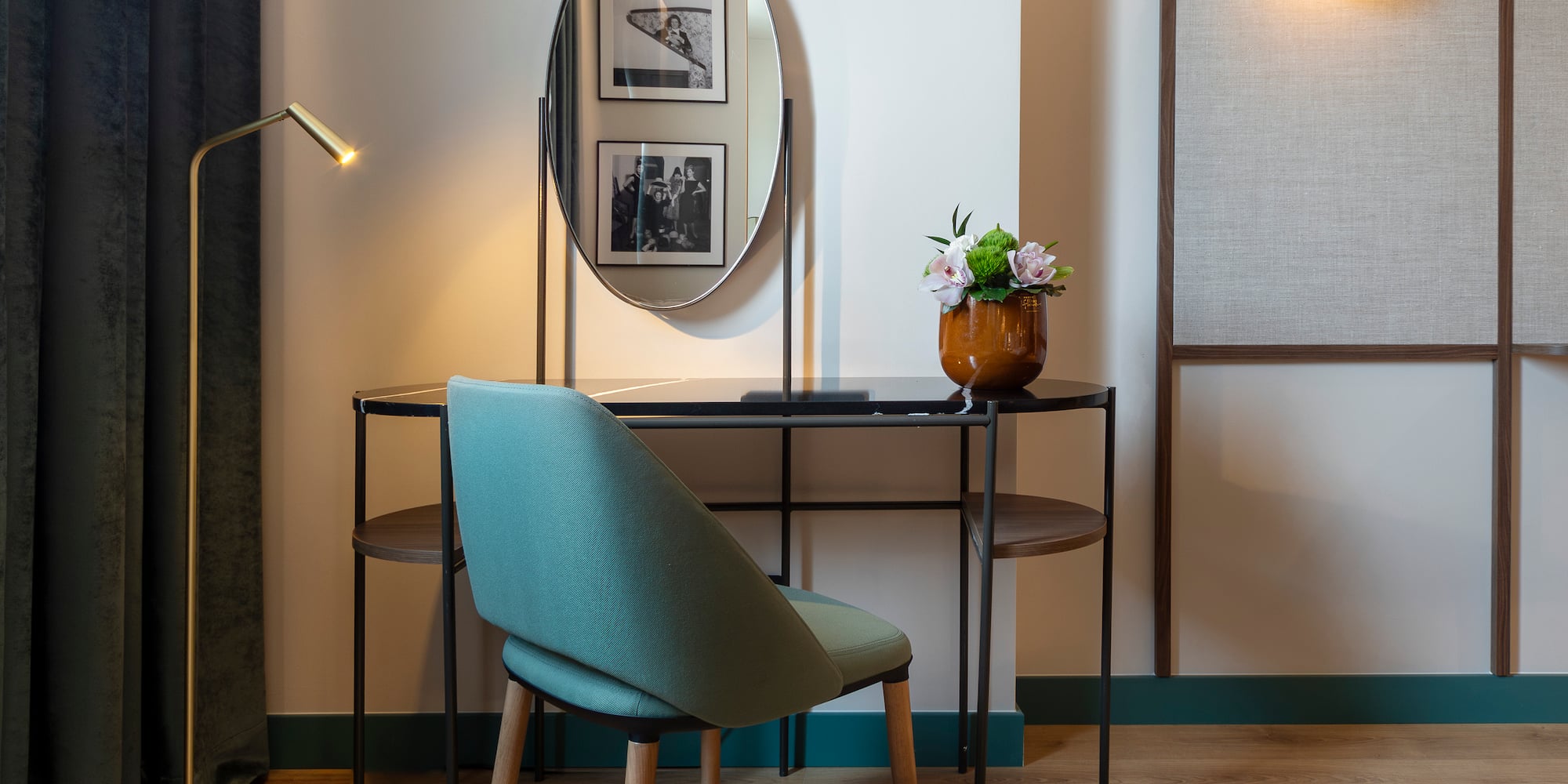 Modern hotel vanity desk with oval mirror, teal chair, and golden lamp.