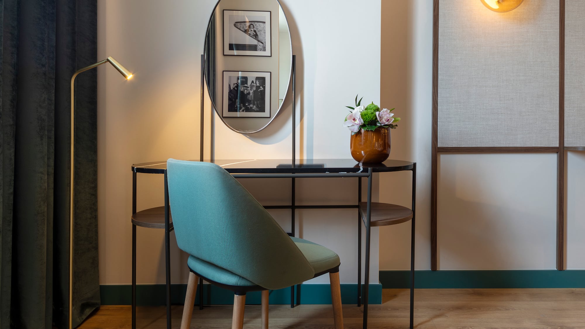 Modern hotel vanity desk with oval mirror, teal chair, and golden lamp.