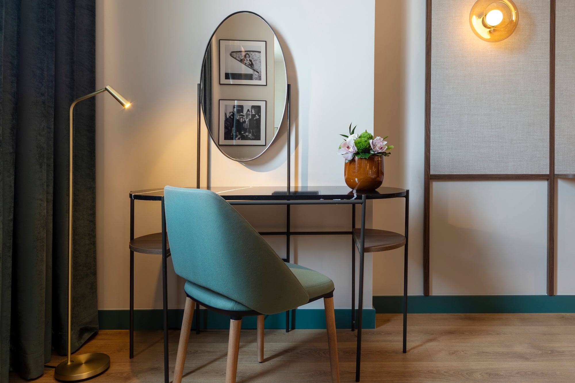 Modern hotel vanity desk with oval mirror, teal chair, and golden lamp.