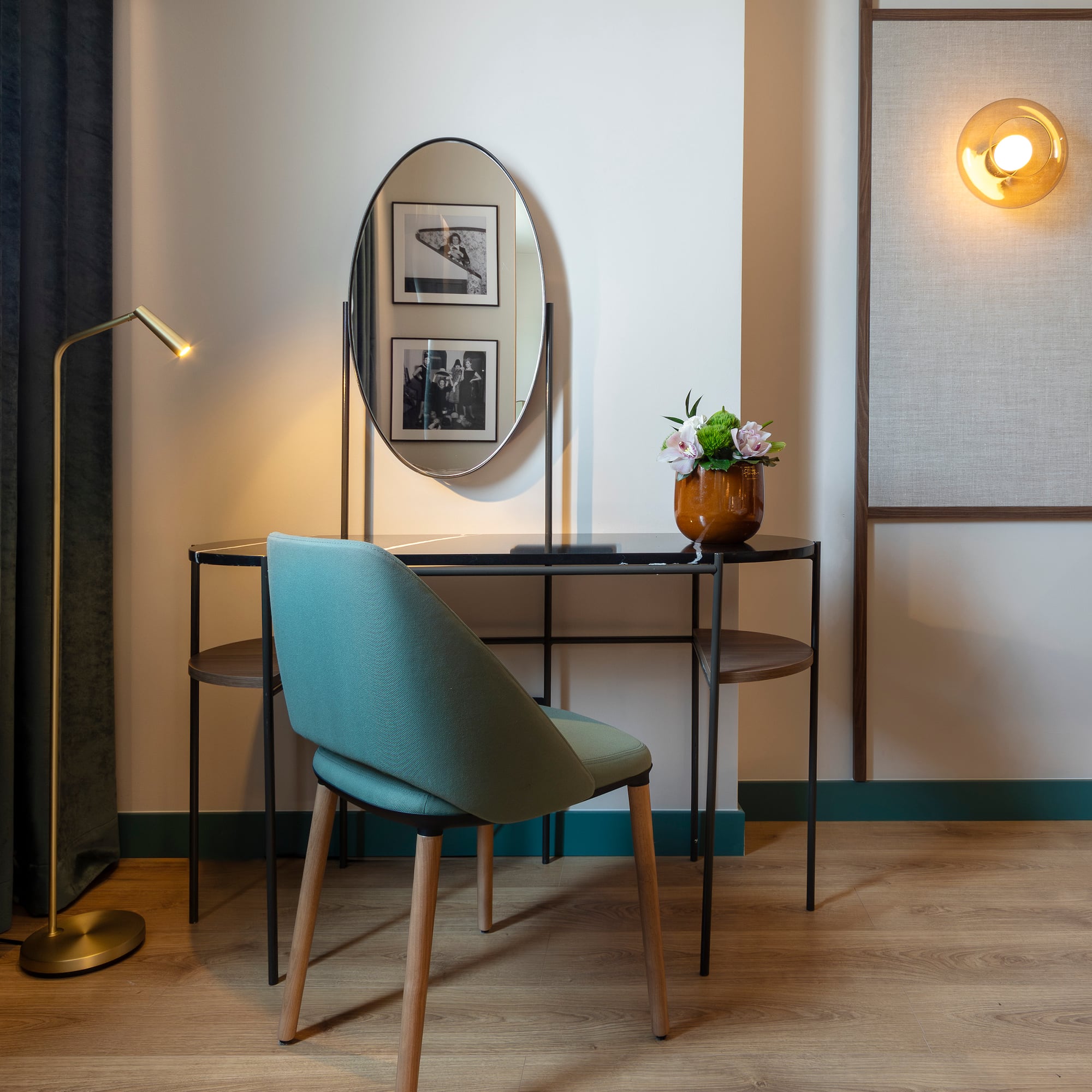Modern hotel vanity desk with oval mirror, teal chair, and golden lamp.