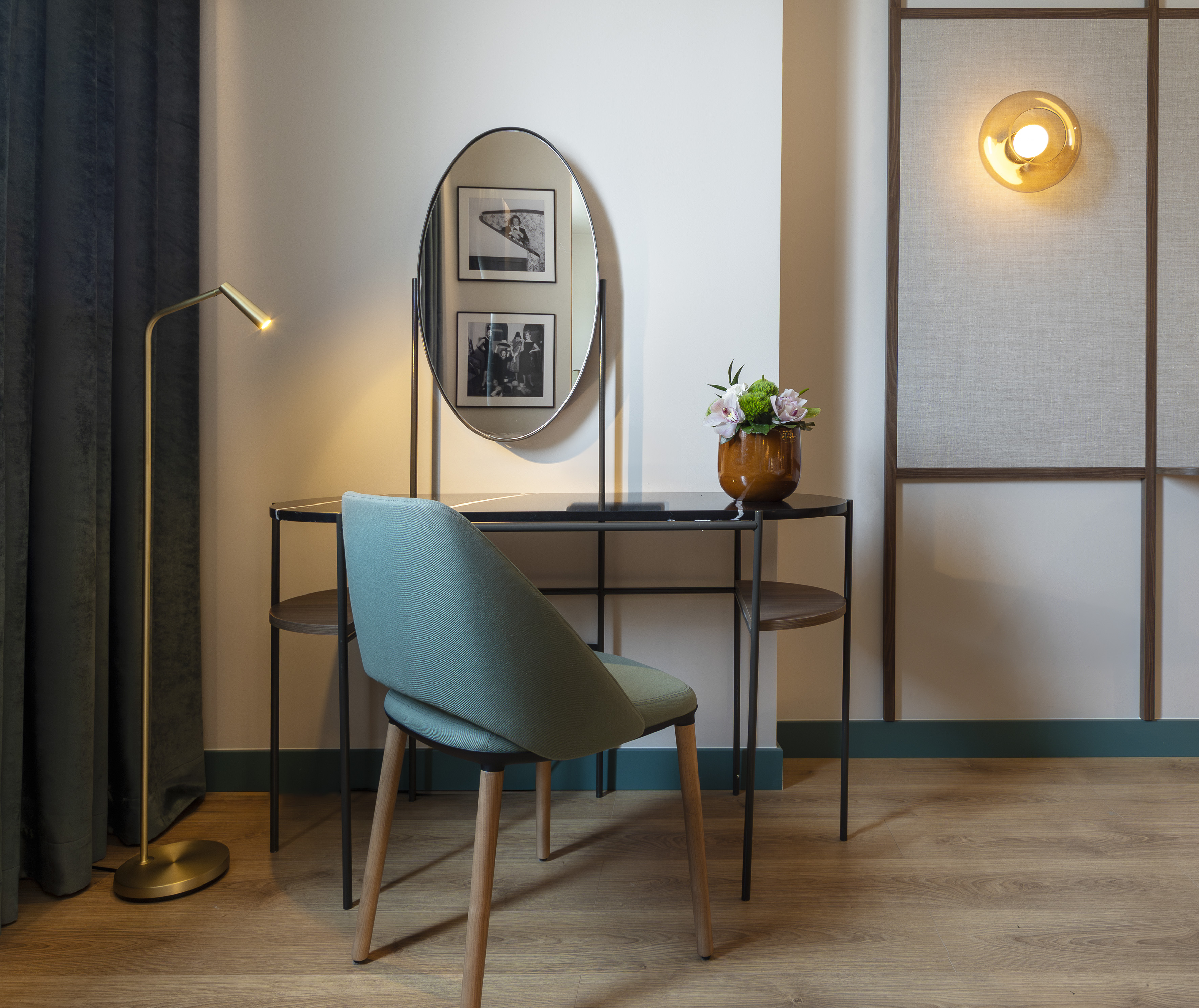 Modern hotel vanity desk with oval mirror, teal chair, and golden lamp.