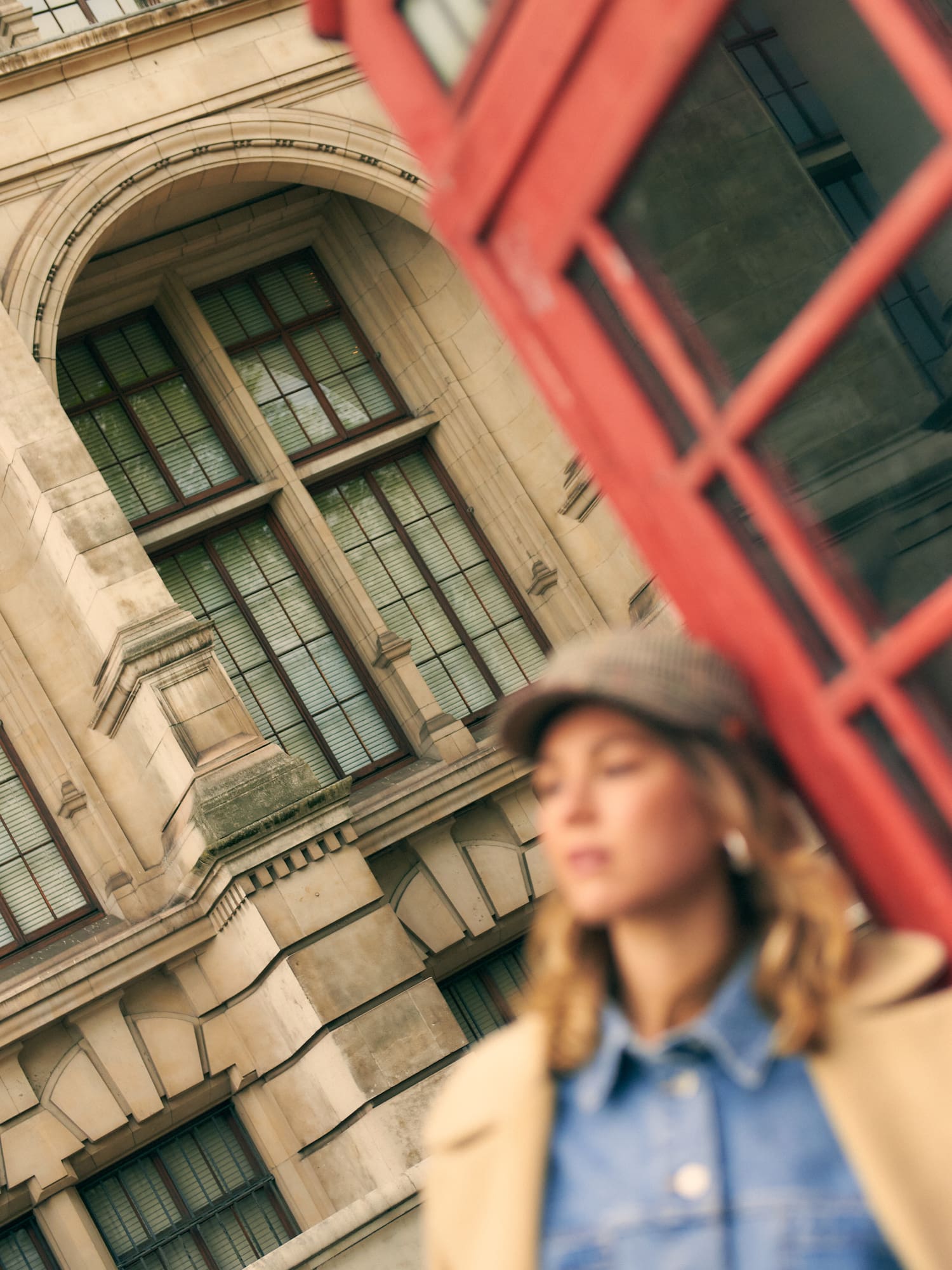 Cabina telefónica roja, edificio londinense, mujer con gorra.