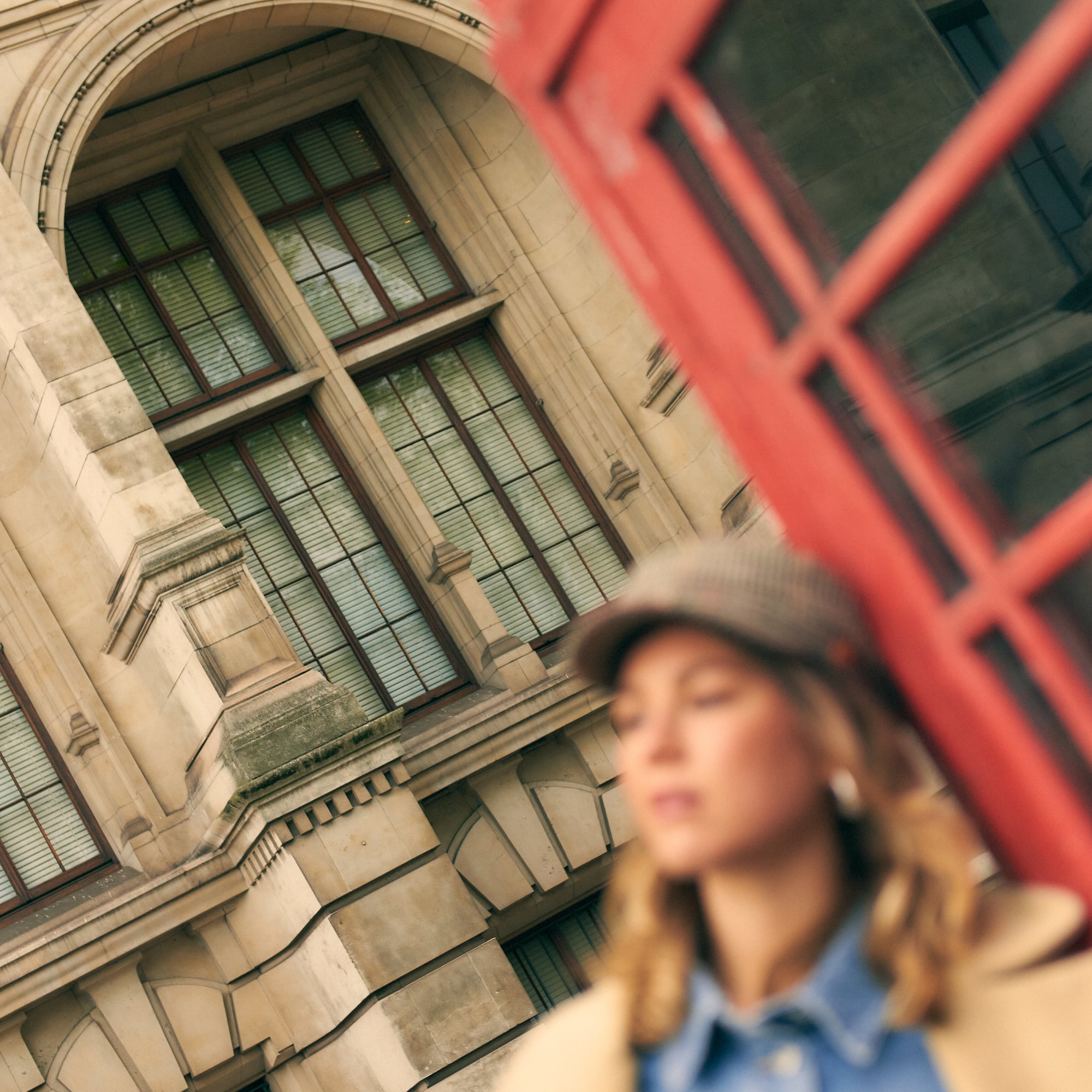 Cabina telefónica roja, edificio londinense, mujer con gorra.