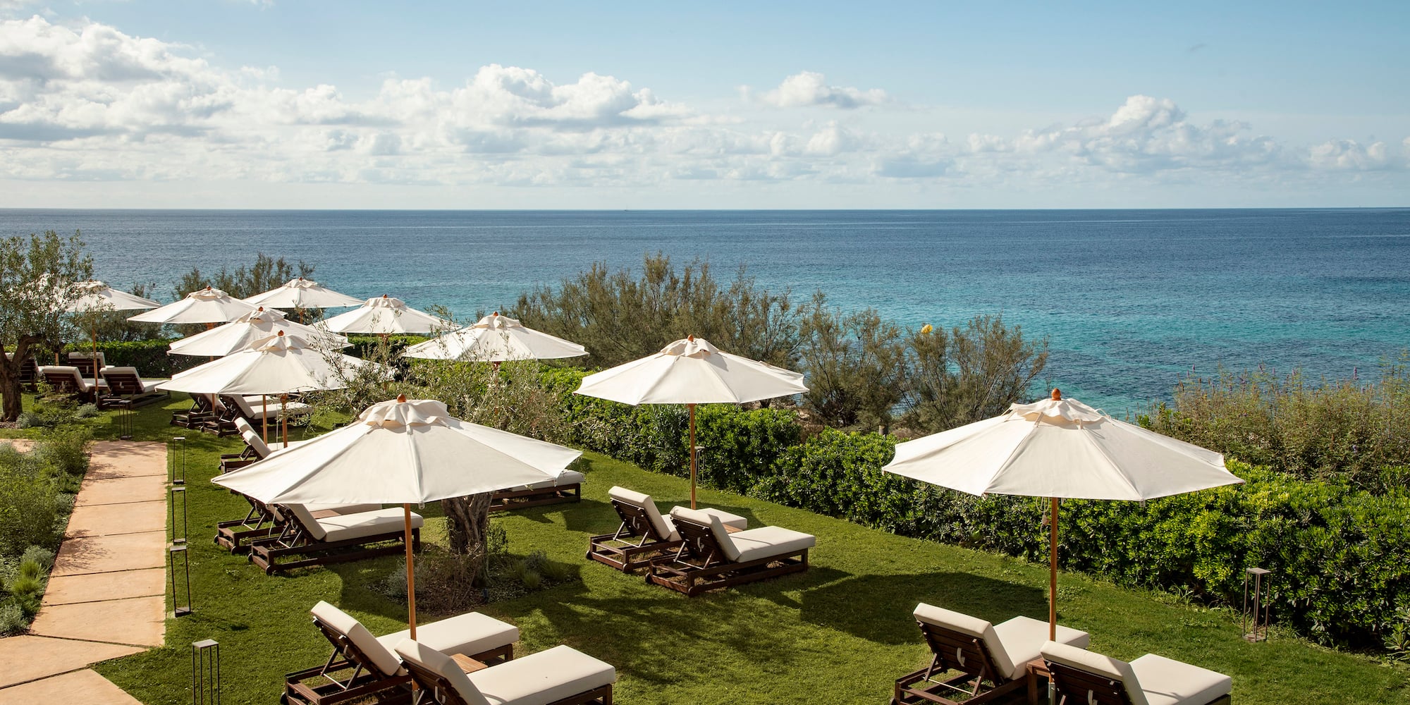 a group of chairs and umbrellas on grass with water in the background