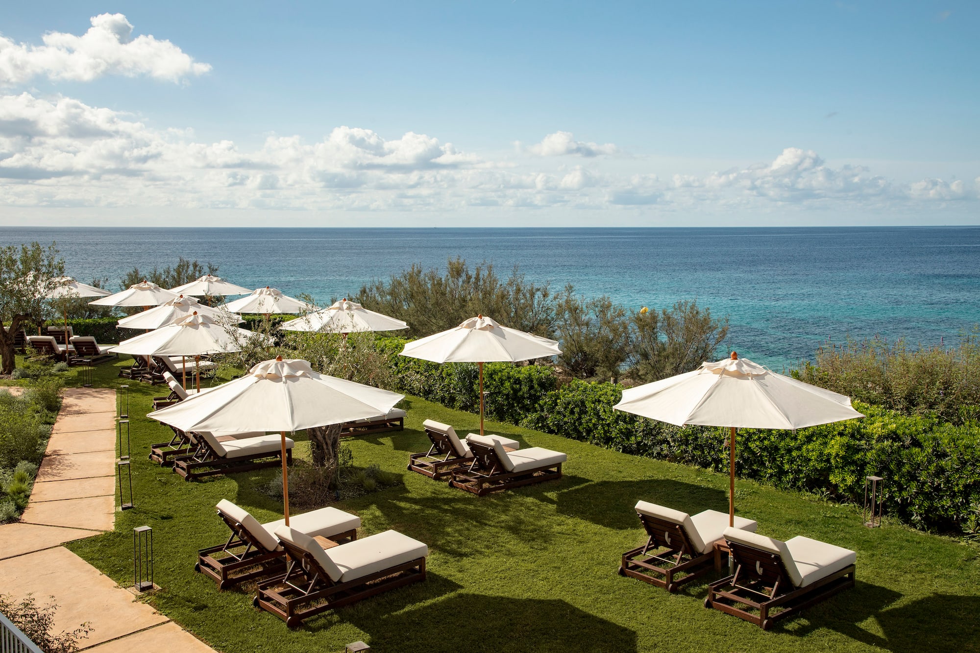 Beach club terrace with white parasols, wooden sunbeds, and turquoise ocean.