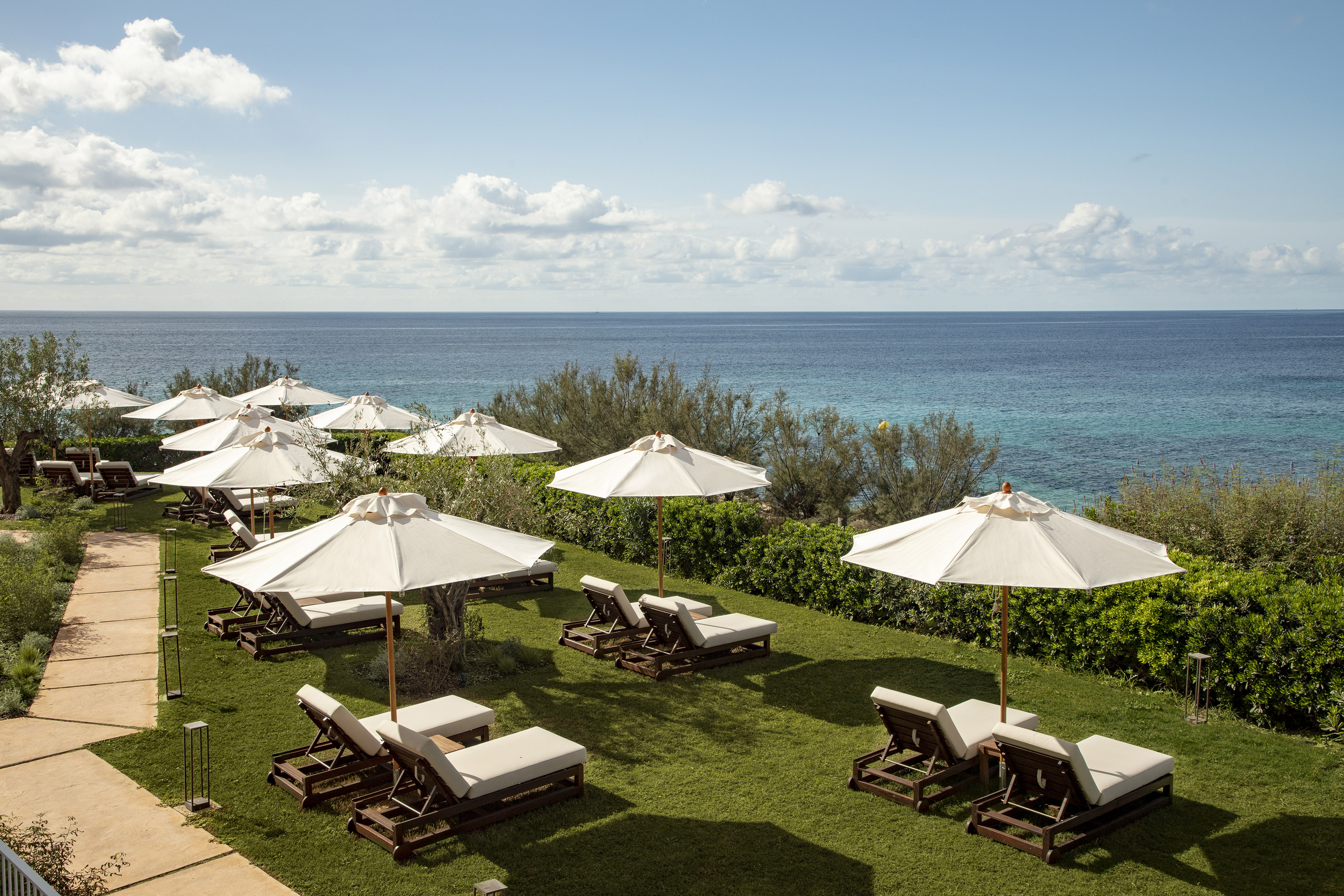 Beach club terrace with white parasols, wooden sunbeds, and turquoise ocean.