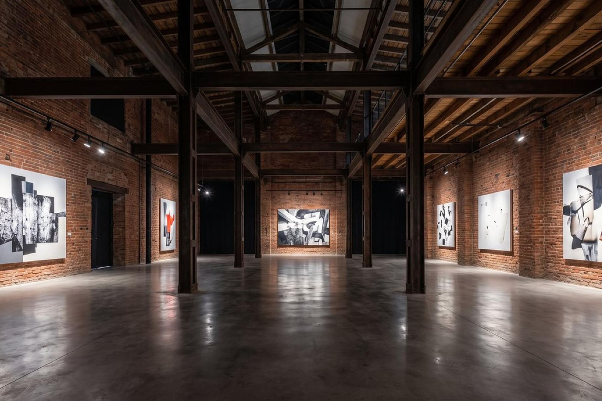 Galería de arte industrial con paredes de ladrillo y pinturas abstractas modernas.
