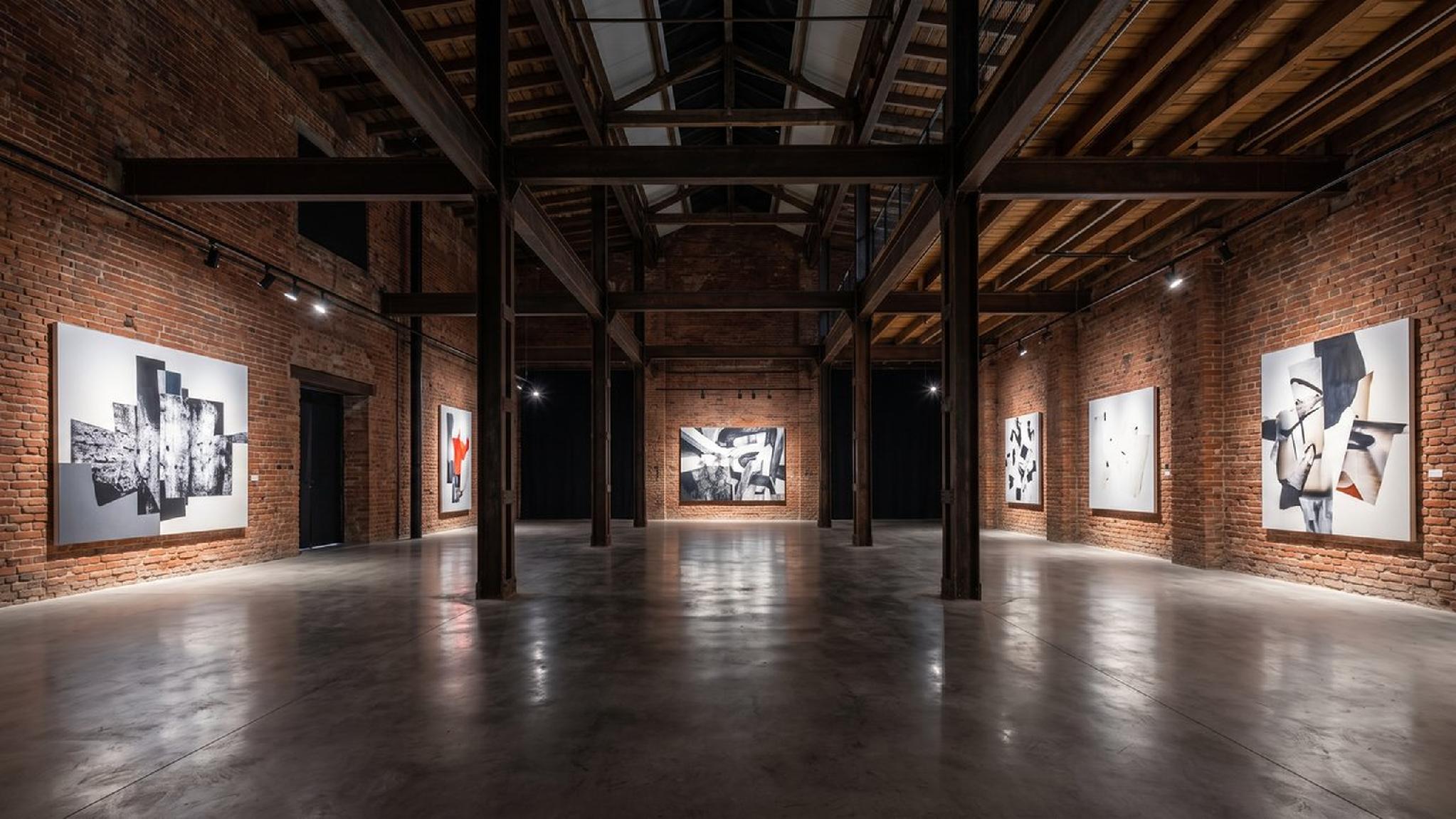 Galería de arte industrial con paredes de ladrillo y pinturas abstractas modernas.