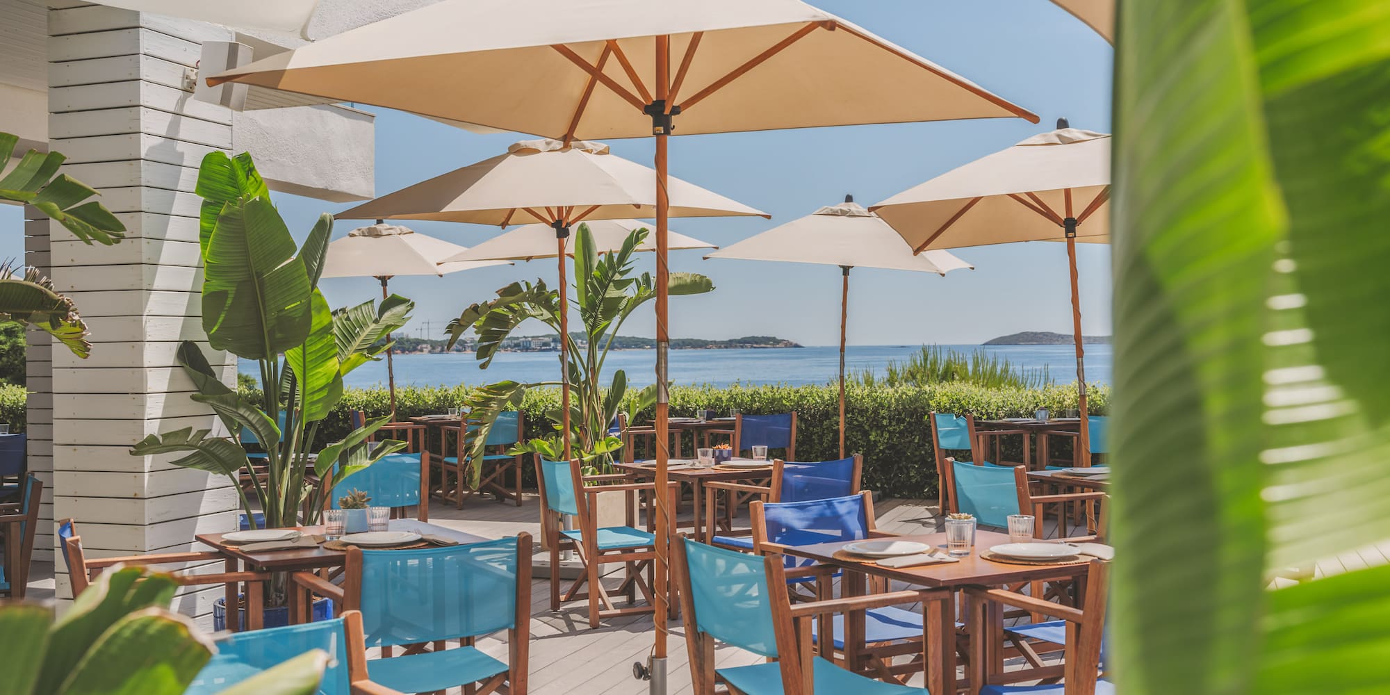 Coastal restaurant terrace with blue chairs, umbrellas, and ocean view.