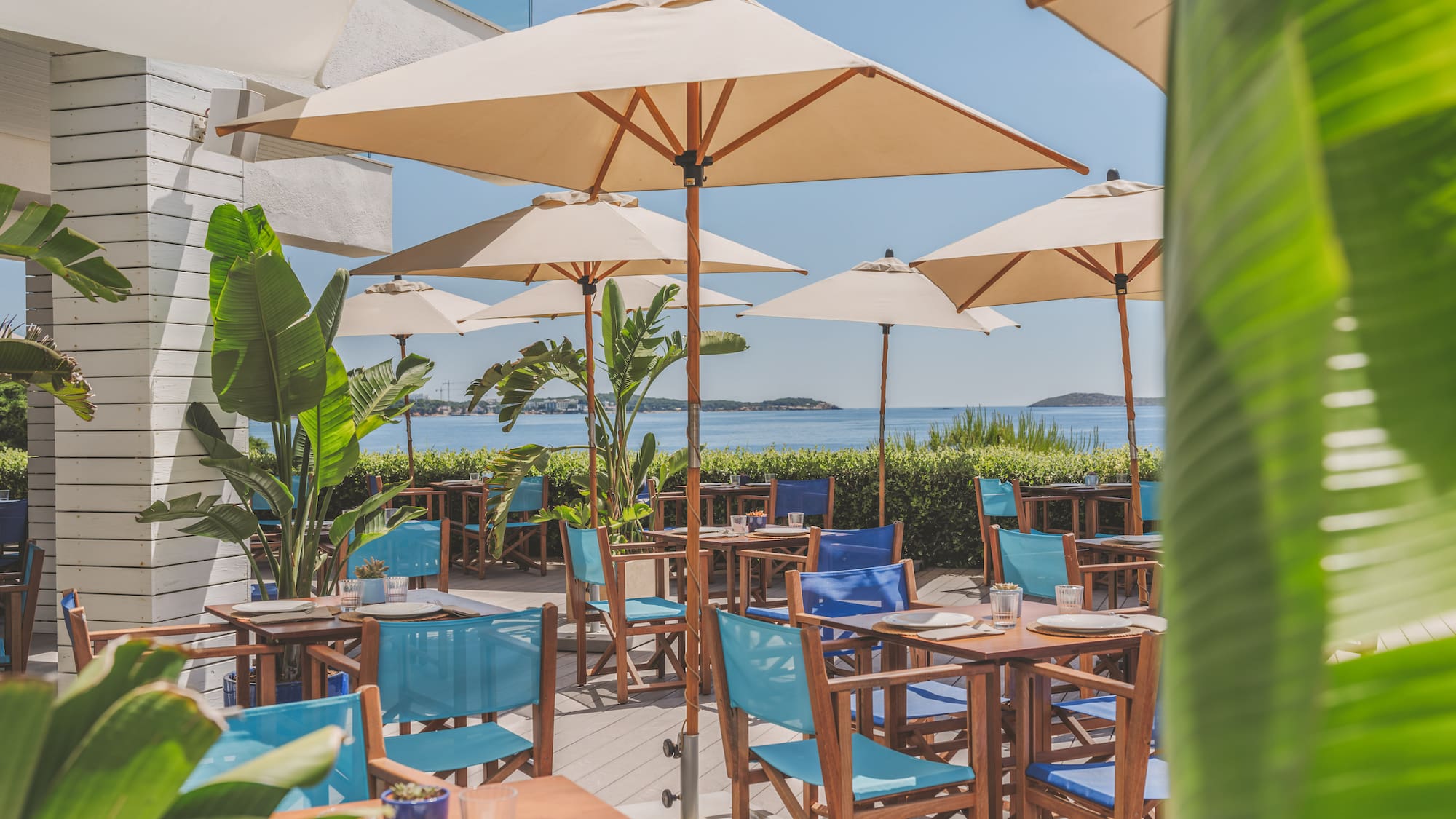 Coastal restaurant terrace with blue chairs, umbrellas, and ocean view.