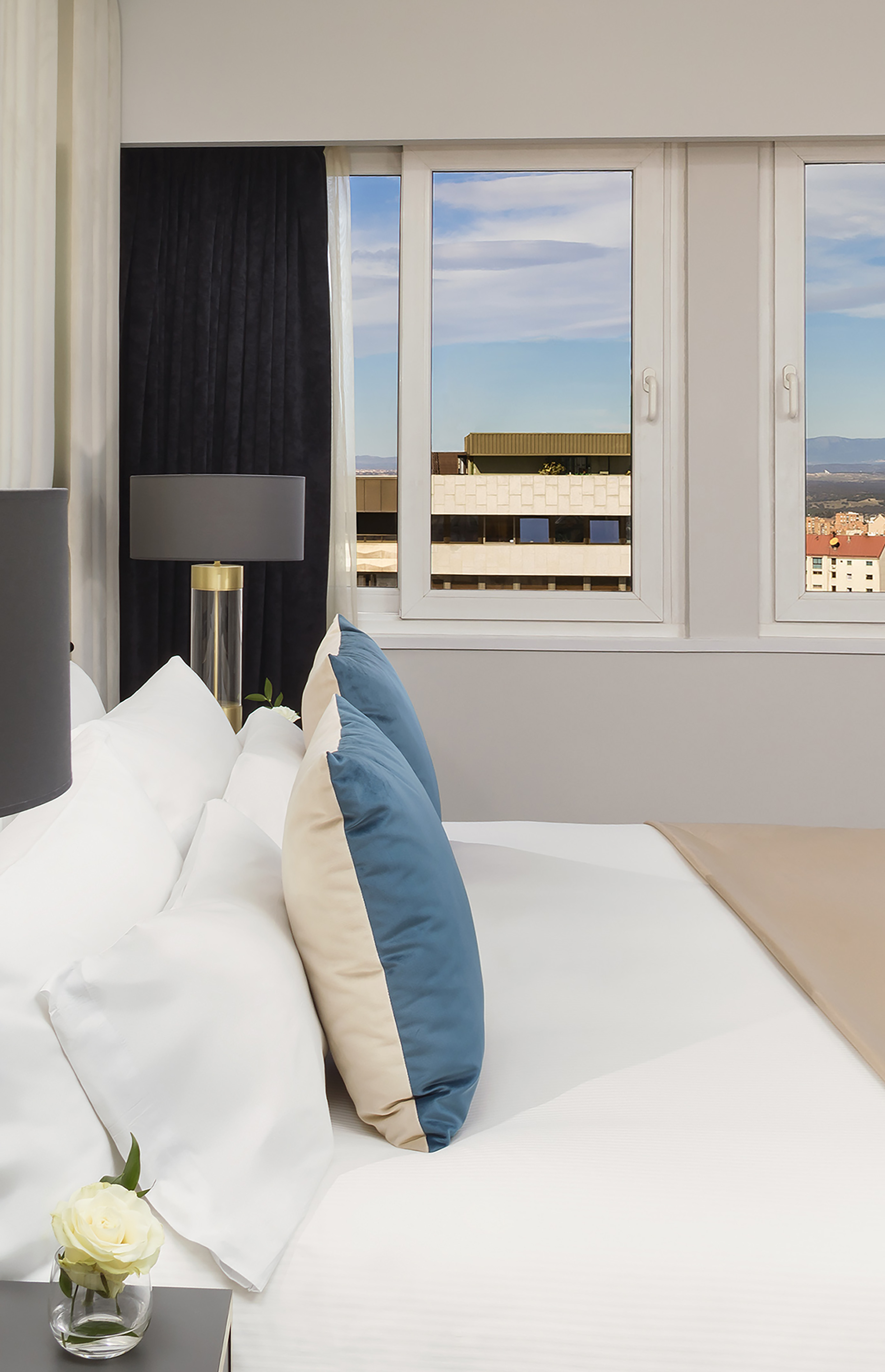 a bed with pillows and a lamp in a room with windows