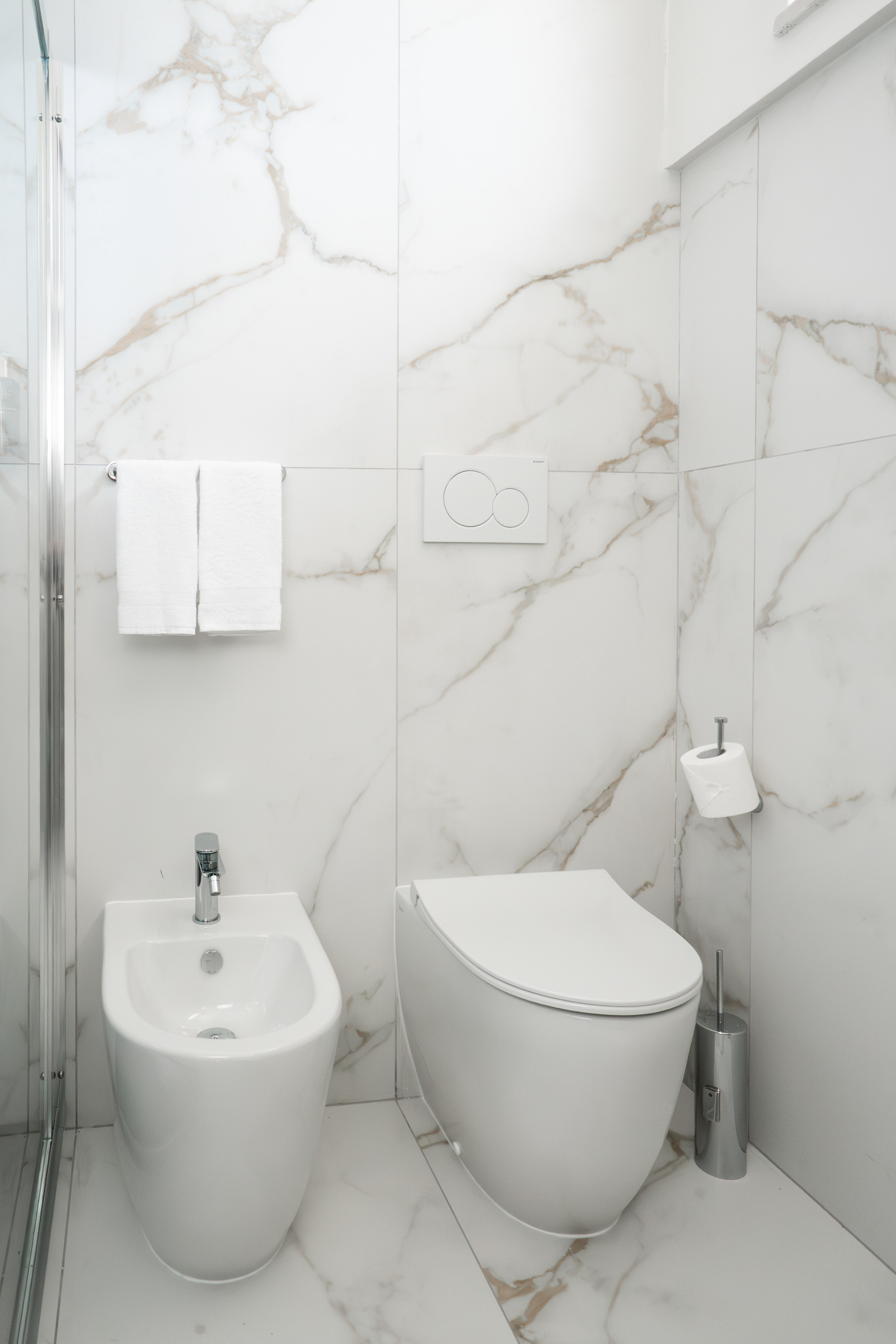 Luxury white marble bathroom featuring a modern toilet and bidet.