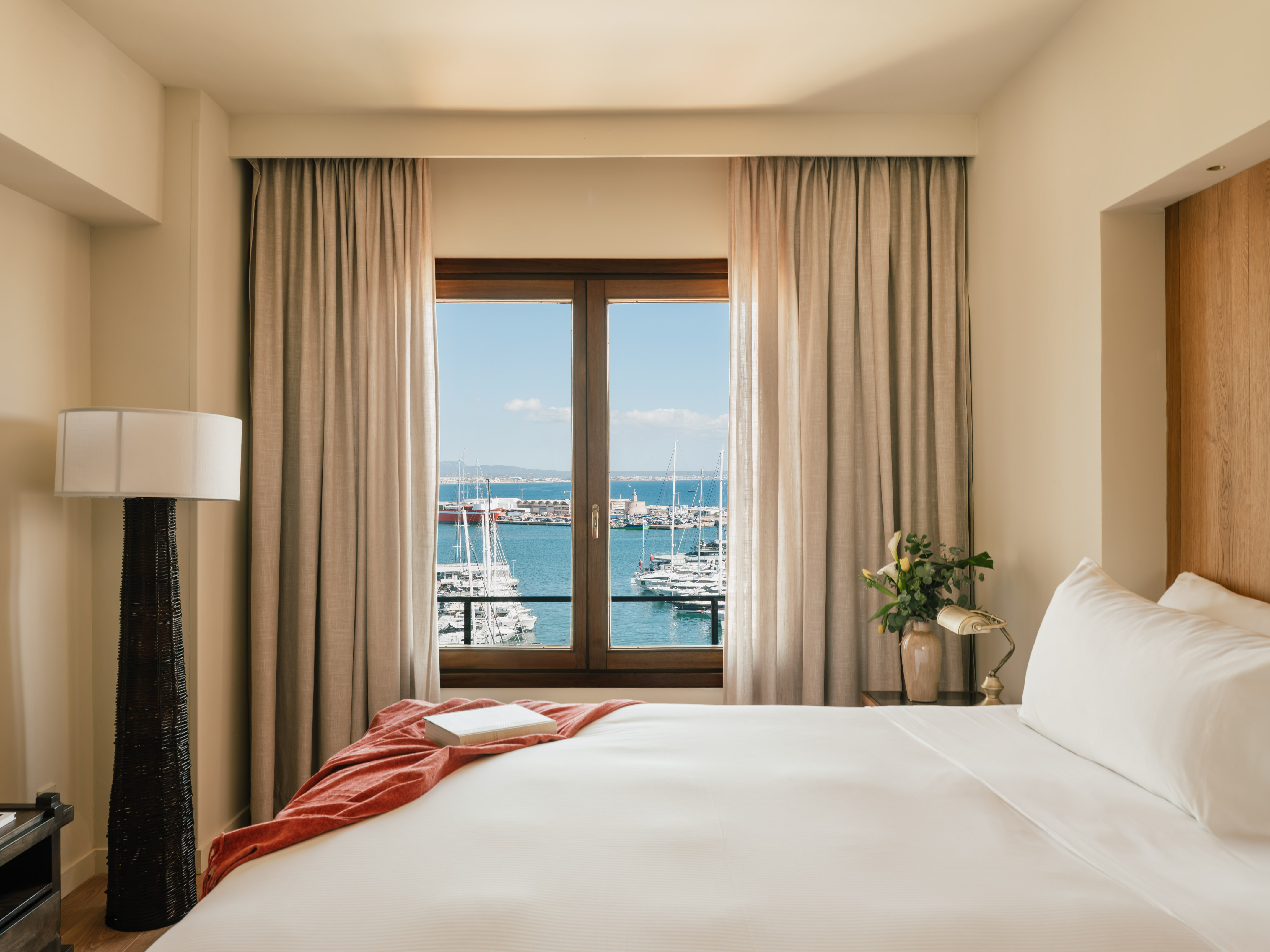 Hotel bedroom with large window overlooking a sunny marina filled with yachts.