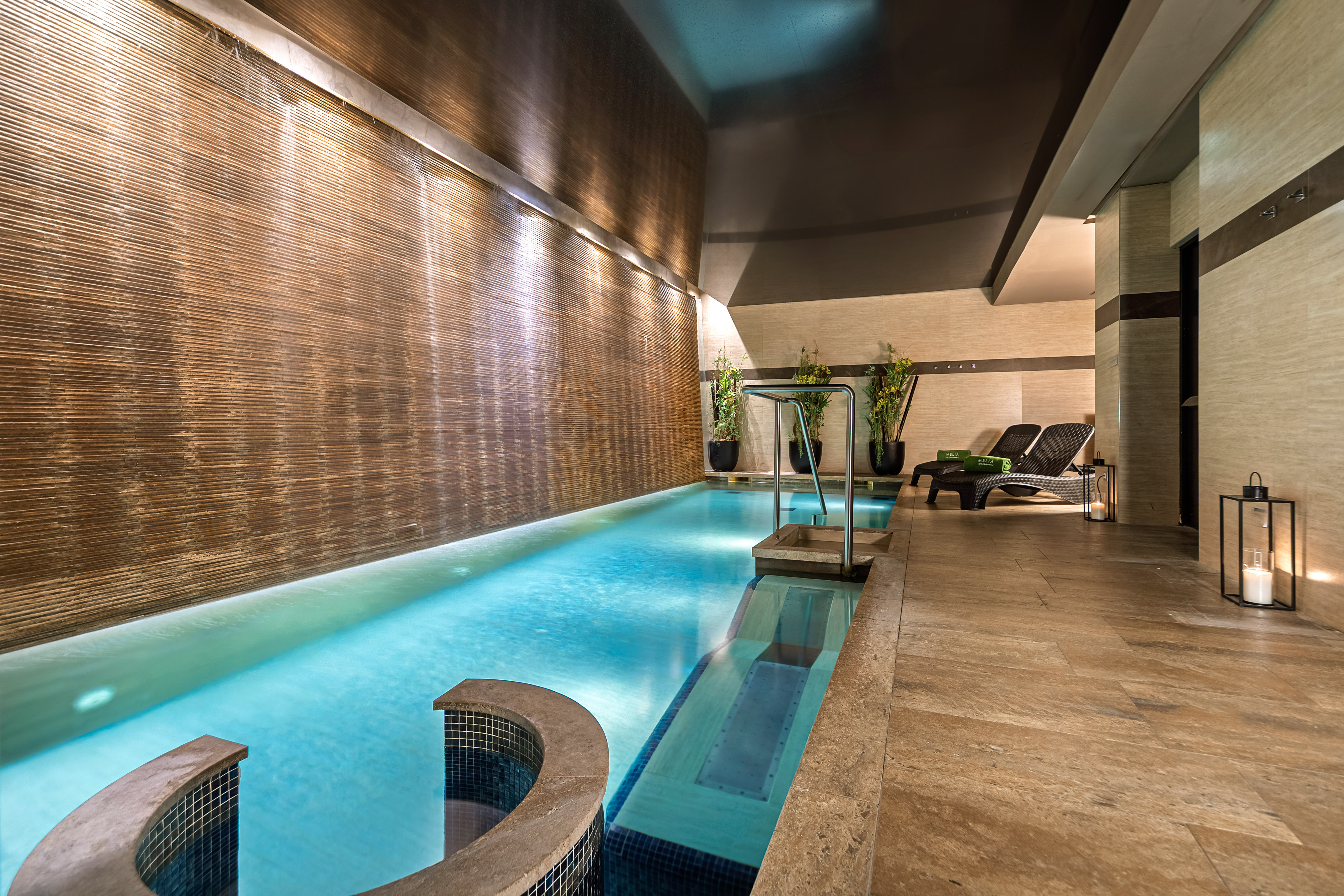Luxurious indoor spa pool with textured waterfall wall and lounge chairs. - Meliá Genova, Genoa