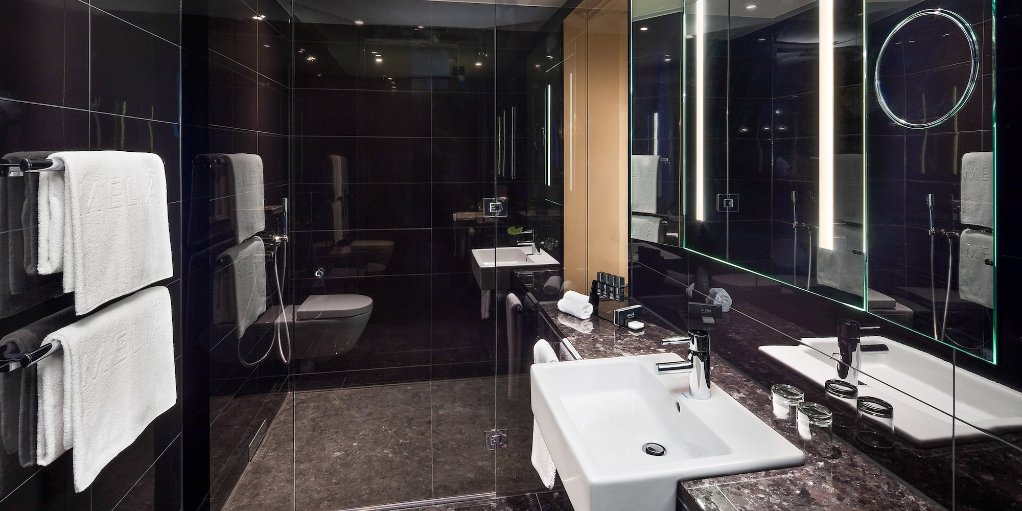 Modern hotel bathroom with black tiles, white sink, and glass shower.