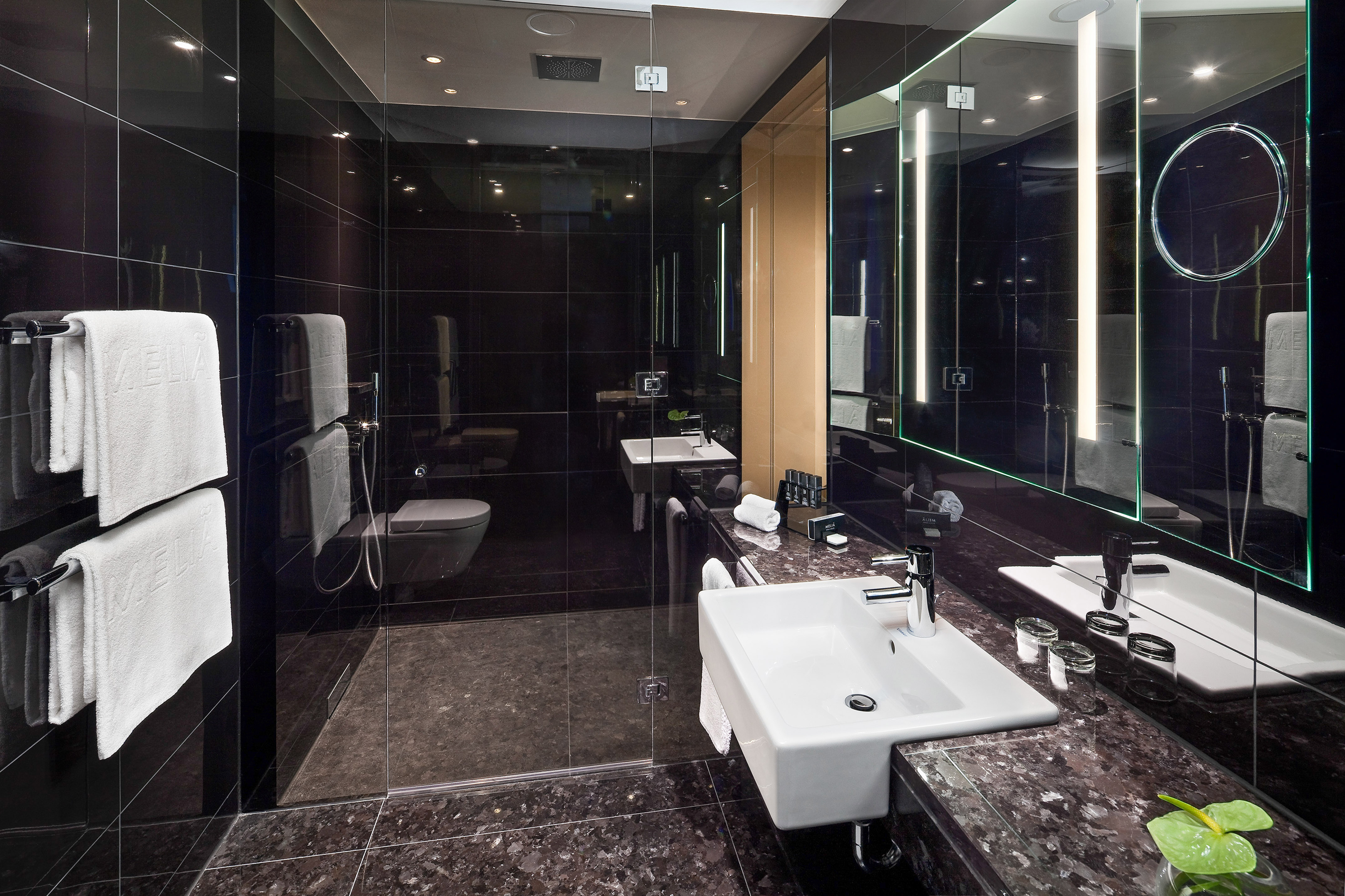 Modern hotel bathroom with black tiles, white sink, and glass shower.