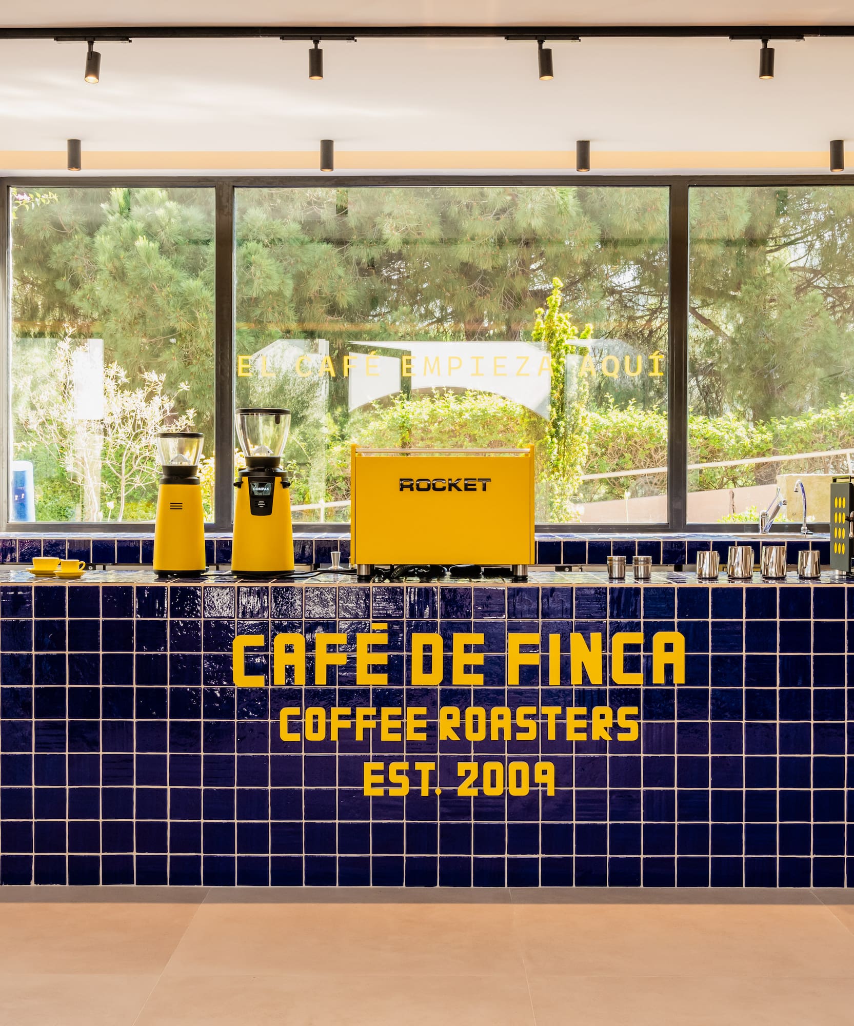 Cafe de Finca coffee bar: blue tiled counter, yellow espresso machine and grinders.