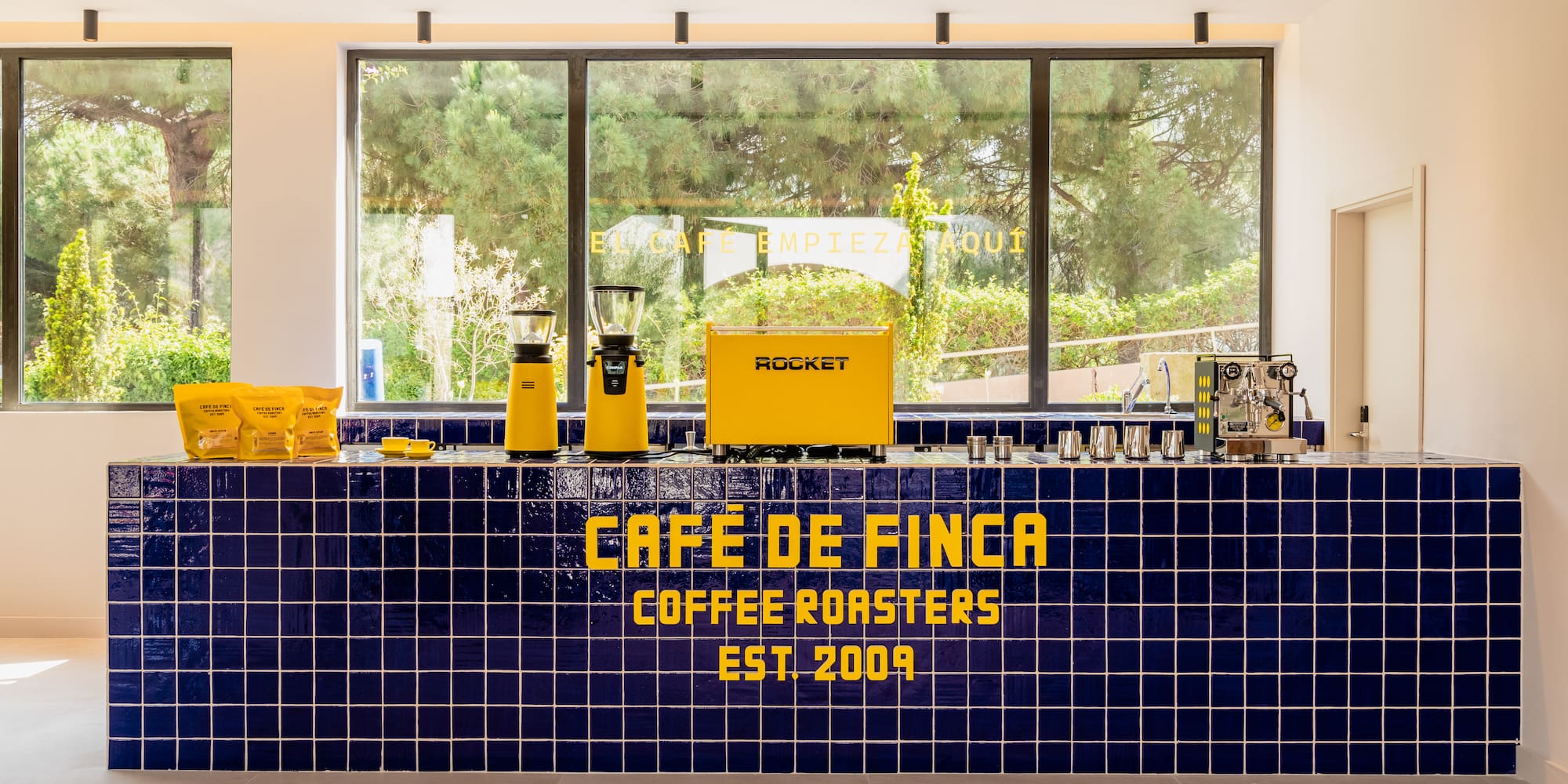Café de Finca coffee roasters bar: blue tiles, yellow espresso machine, grinders.