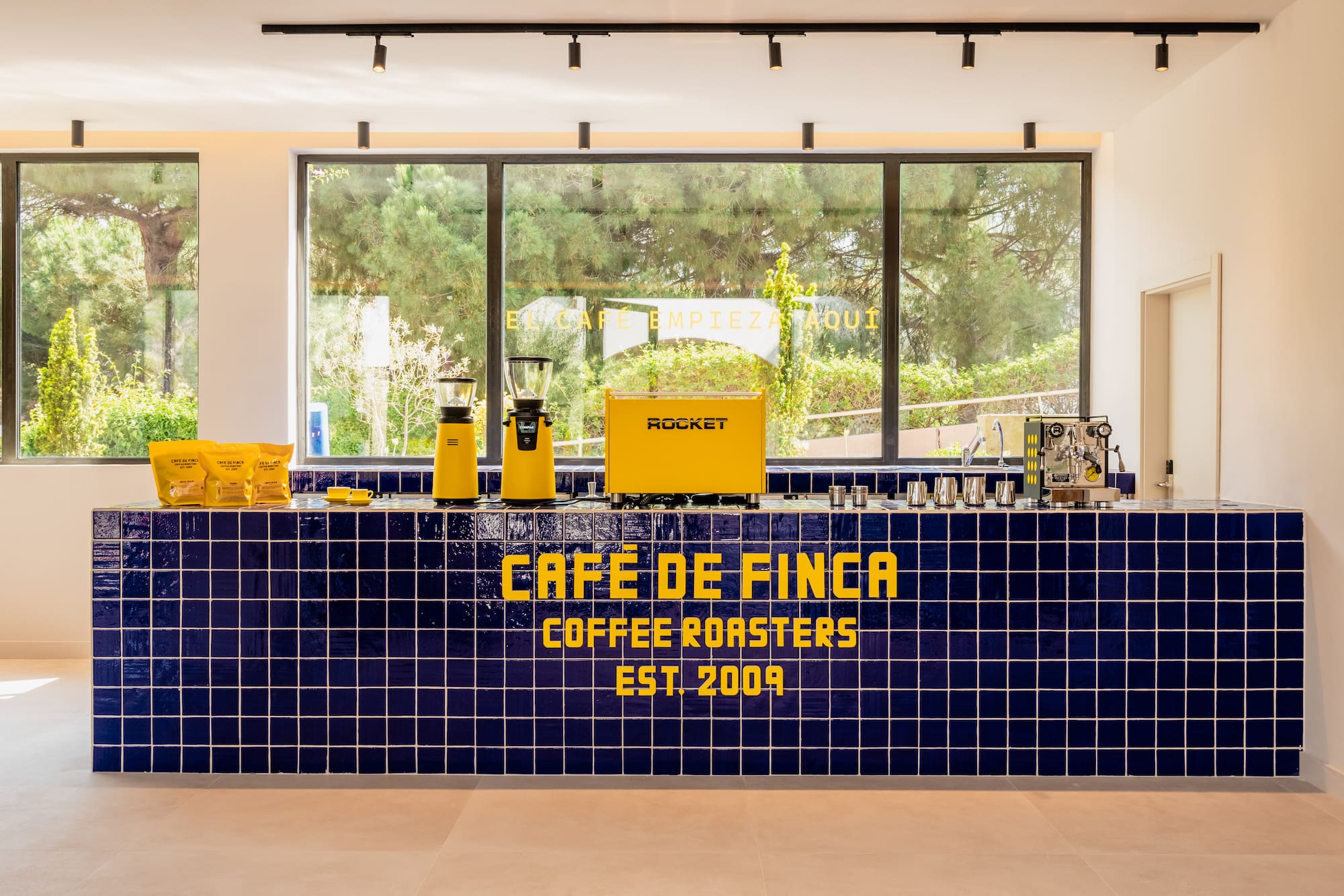 Café de Finca coffee roasters bar: blue tiles, yellow espresso machine, grinders.