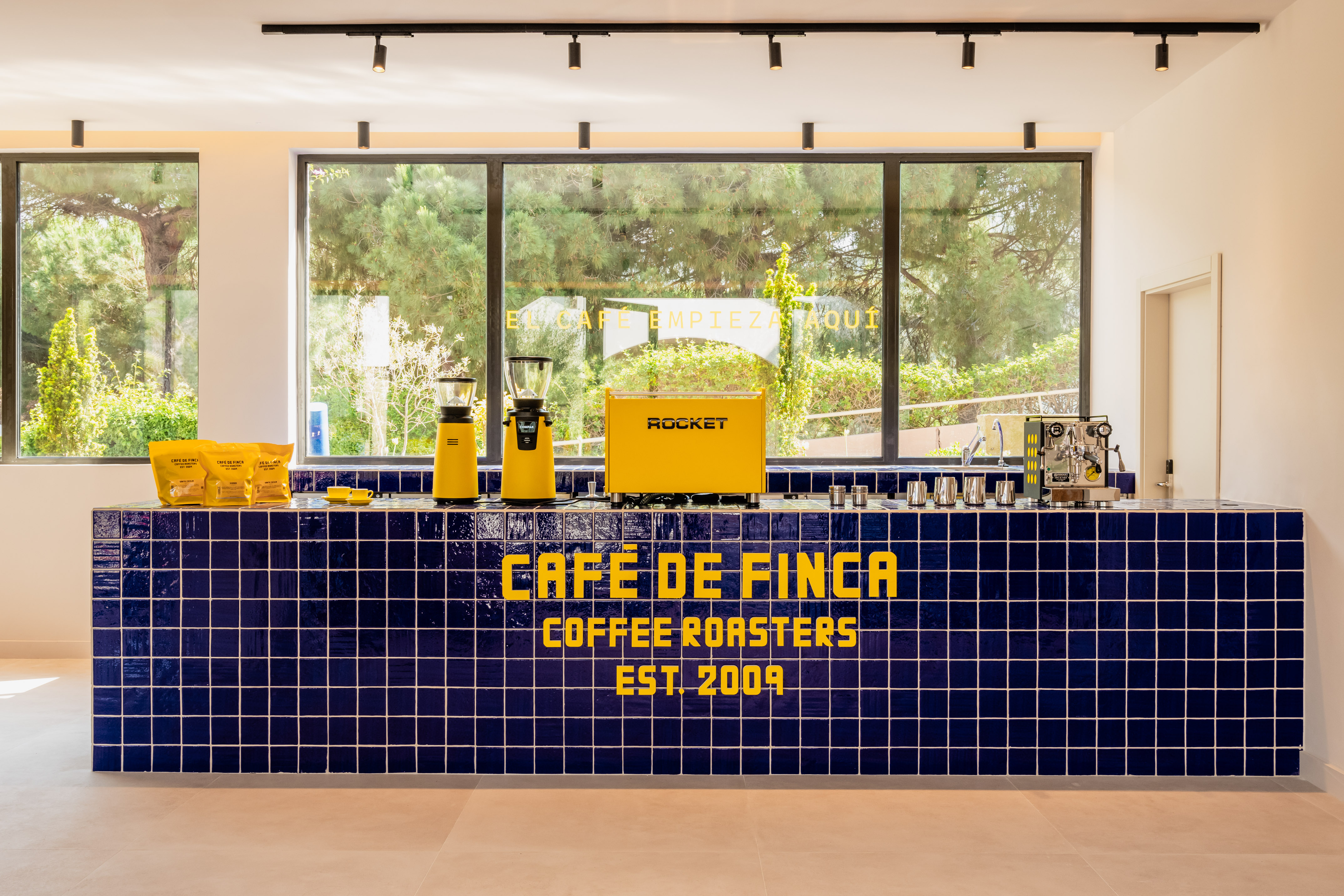 Café de Finca coffee roasters bar: blue tiles, yellow espresso machine, grinders.