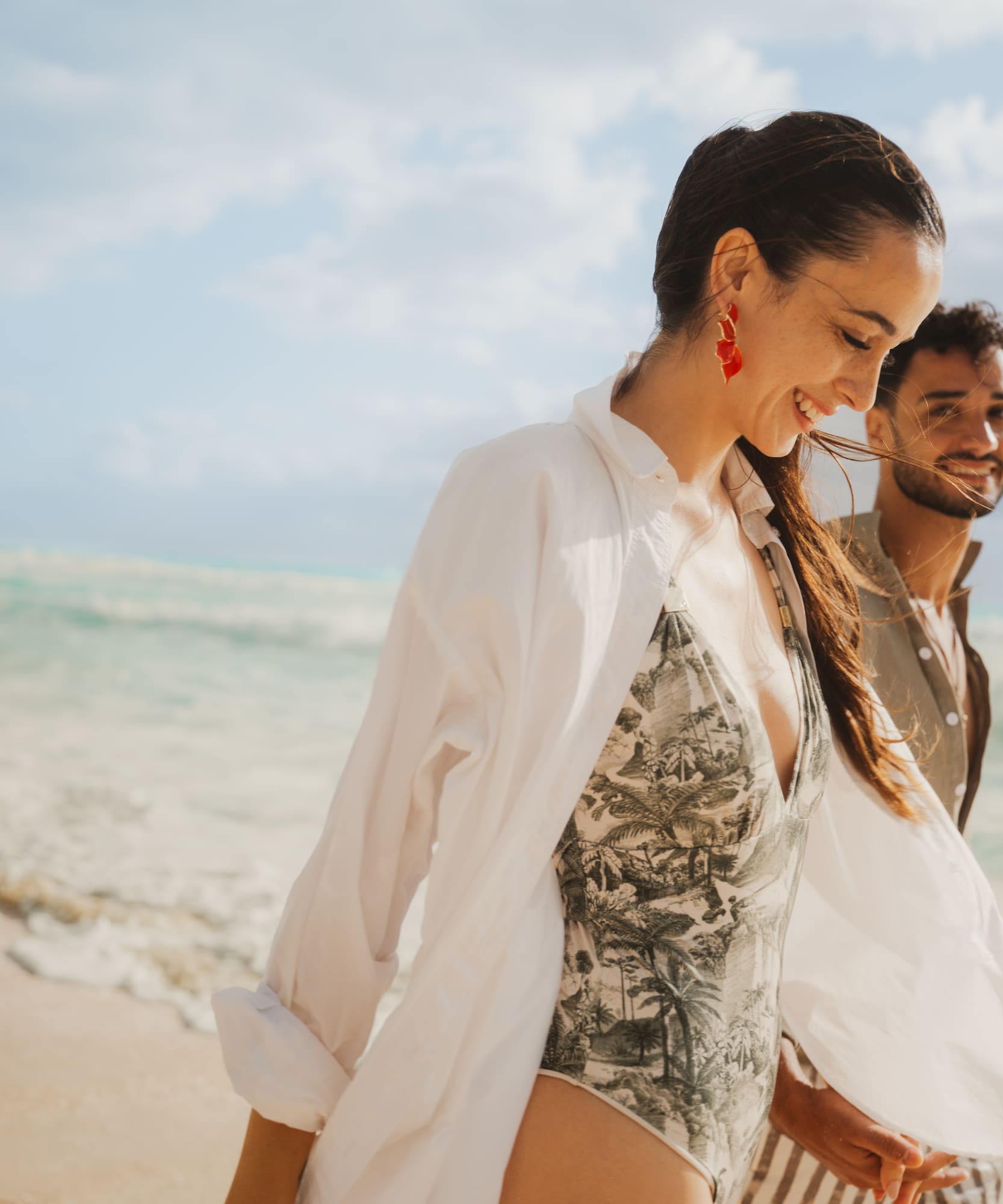 Smiling couple walking on tropical beach with ocean waves.