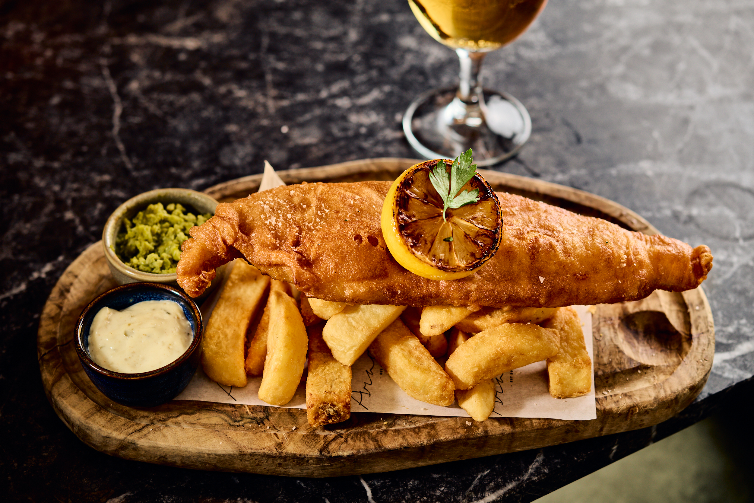 Golden fried fish and chips with lemon, mushy peas, tartar sauce, and beer.