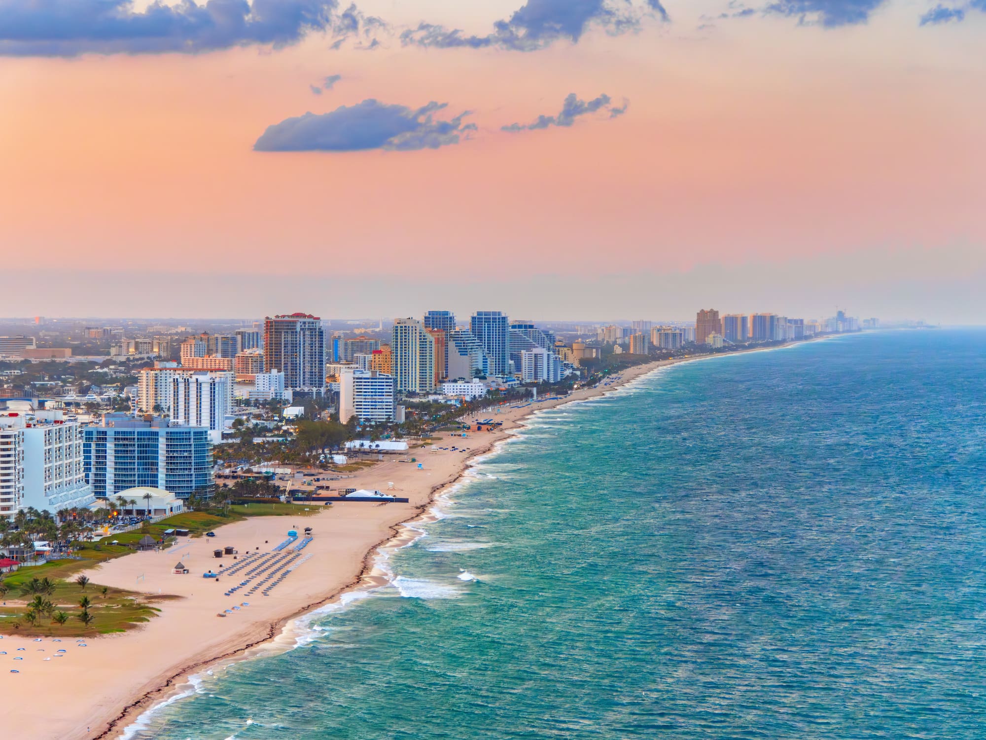 Fort Lauderdale oceanfront skyline, sandy beach, turquoise sea, and sunset sky.