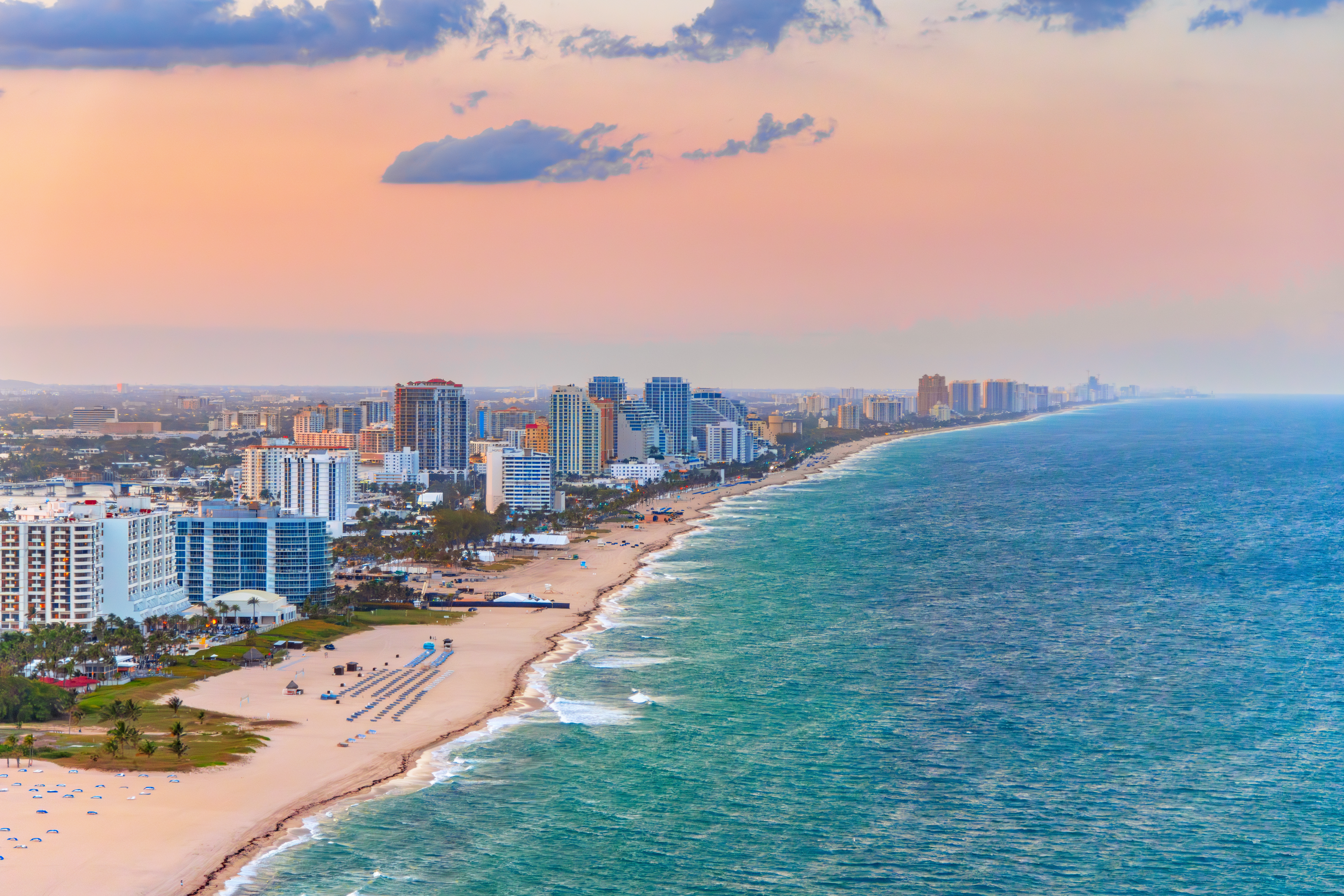 Playa urbana, hoteles altos, mar turquesa y cielo atardecer.