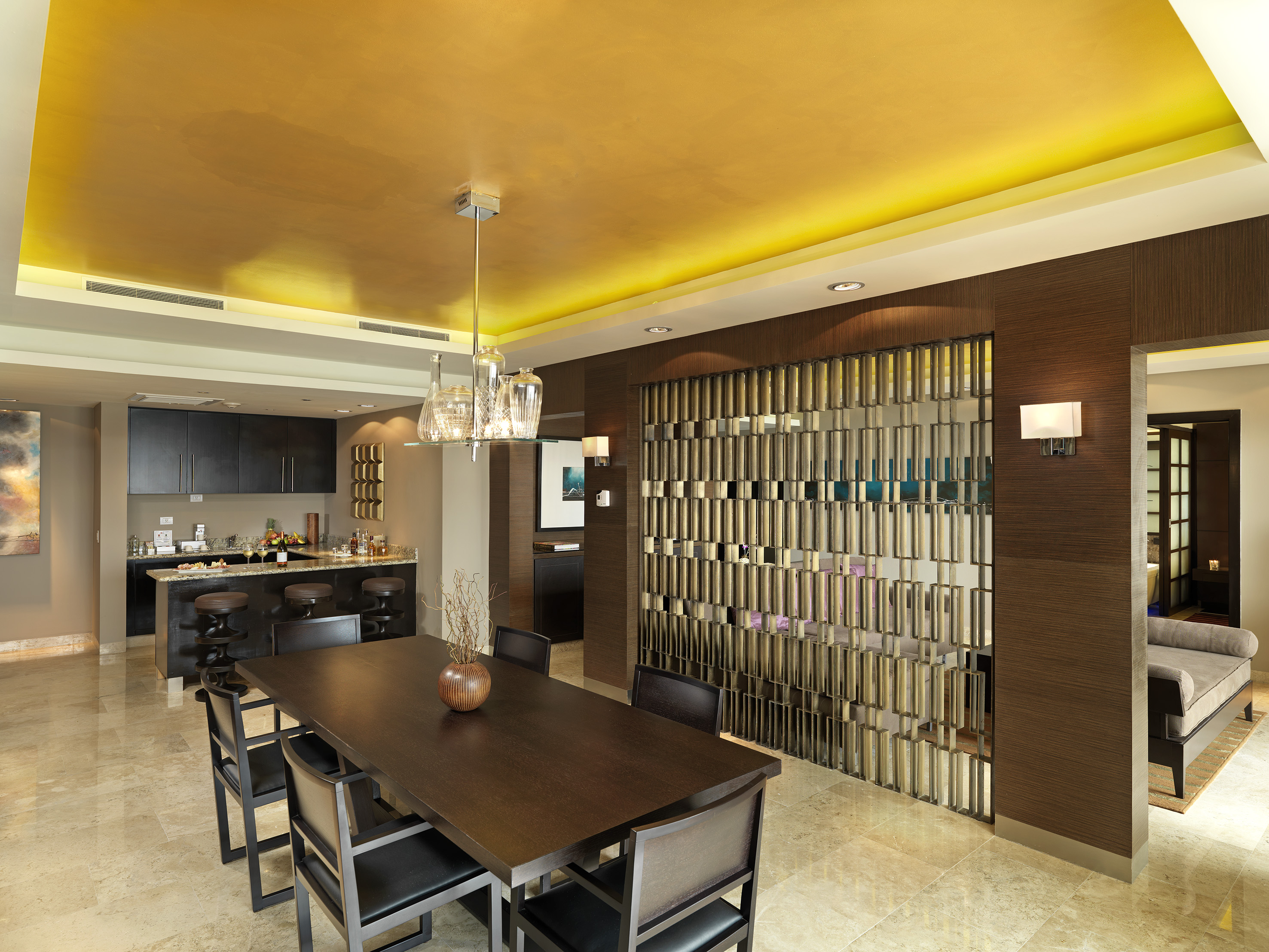 Modern dining room with golden ceiling, dark table, bar, and decorative screen.