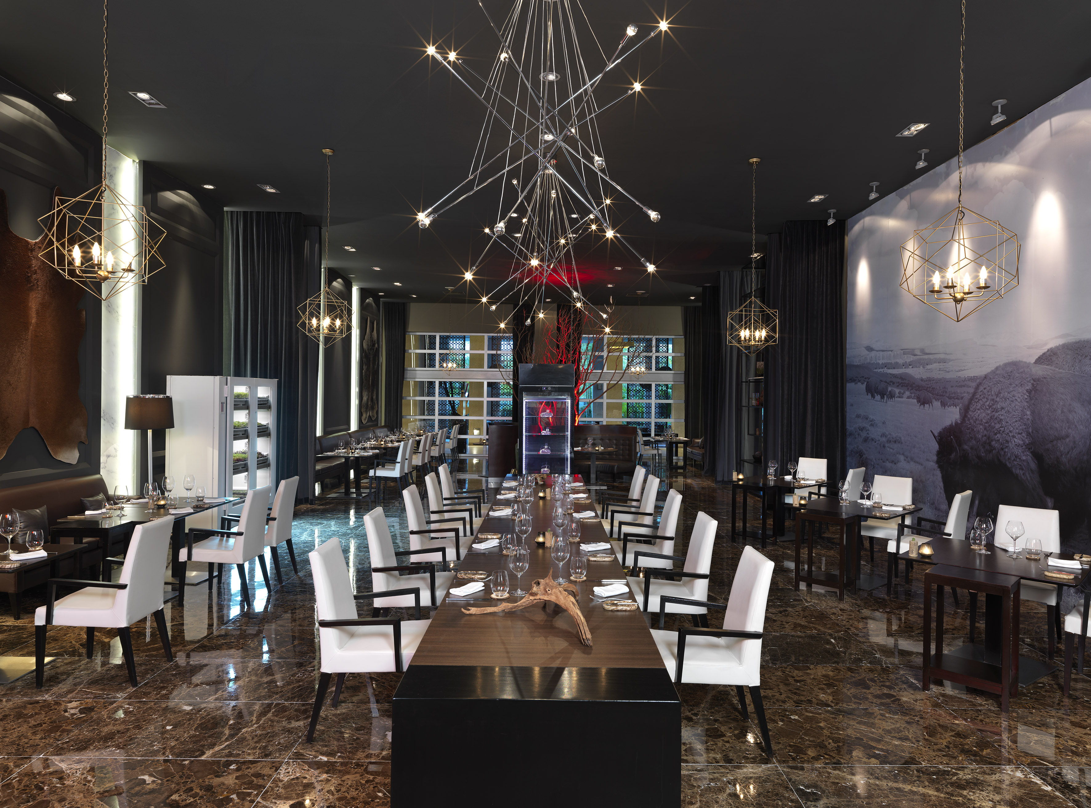 Elegant restaurant with long table, white chairs, and striking chandeliers.