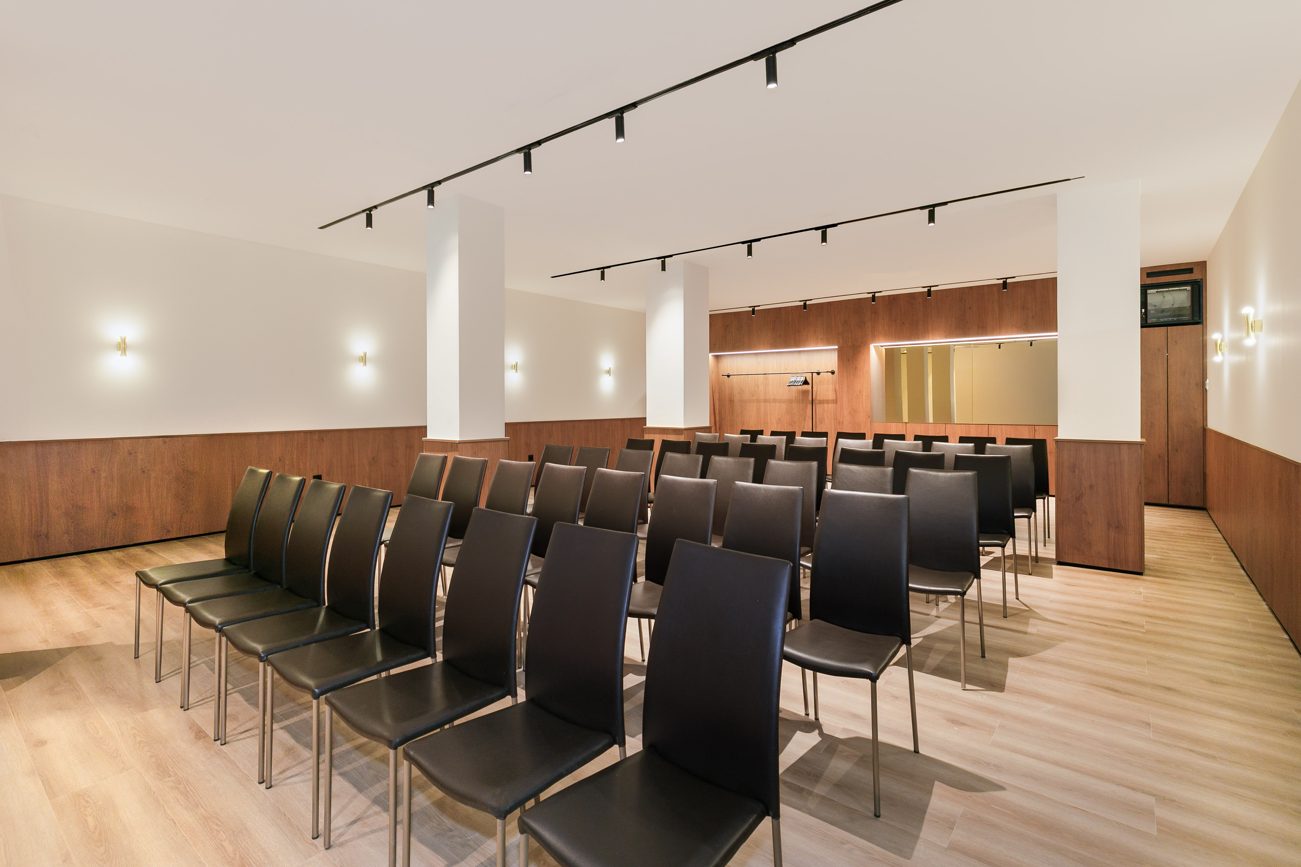 Empty modern meeting room with black chairs, wood accents, and track lighting.