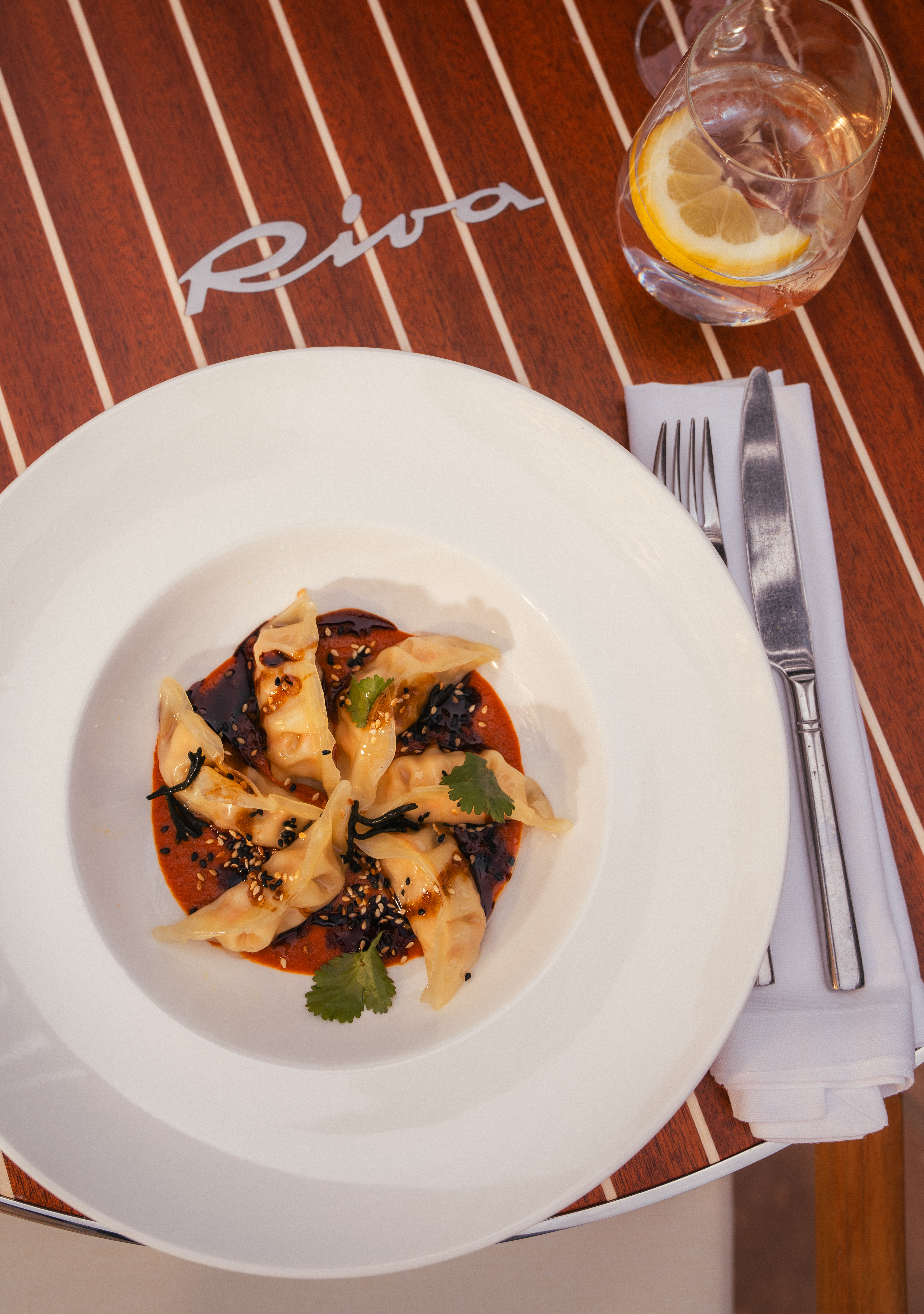 Dumplings in chili oil with sesame and cilantro on a Riva wooden table.