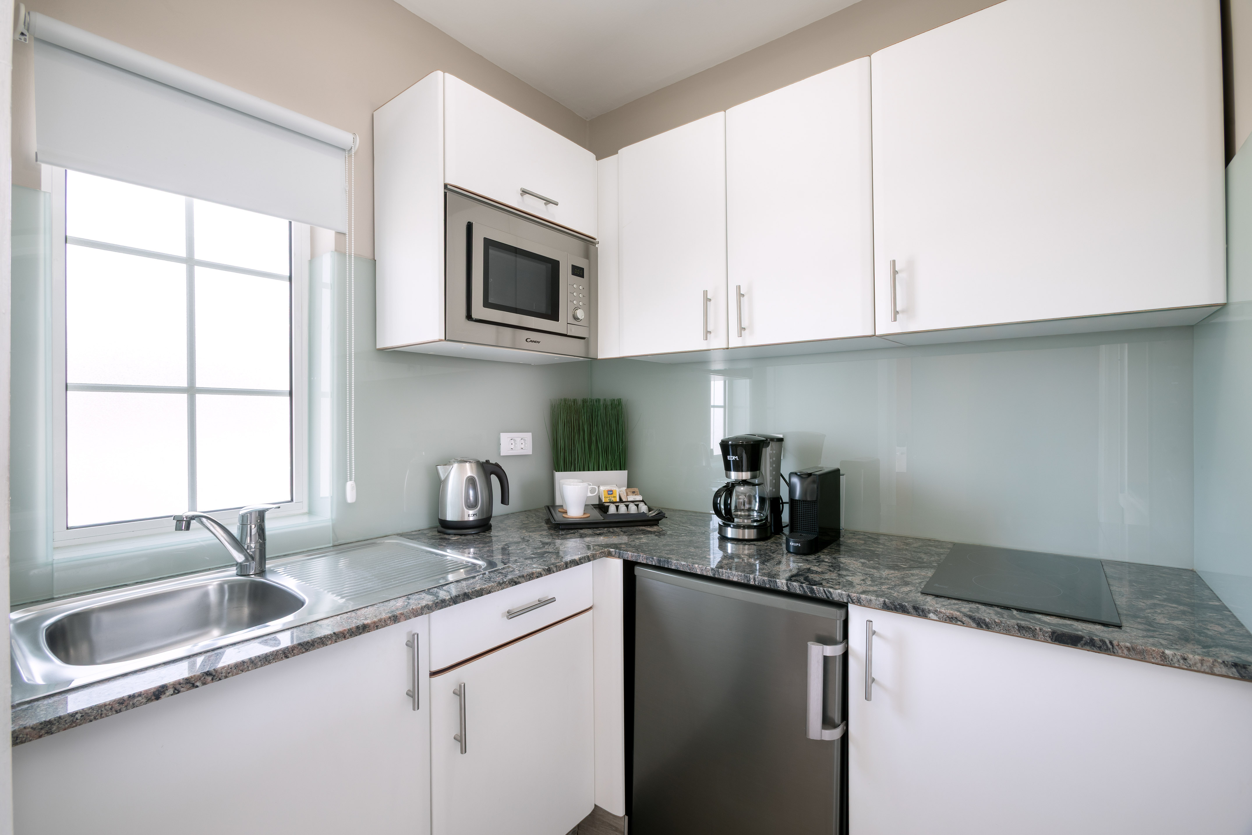 Modern kitchenette with white cabinets, granite counter, microwave, coffee maker, sink.